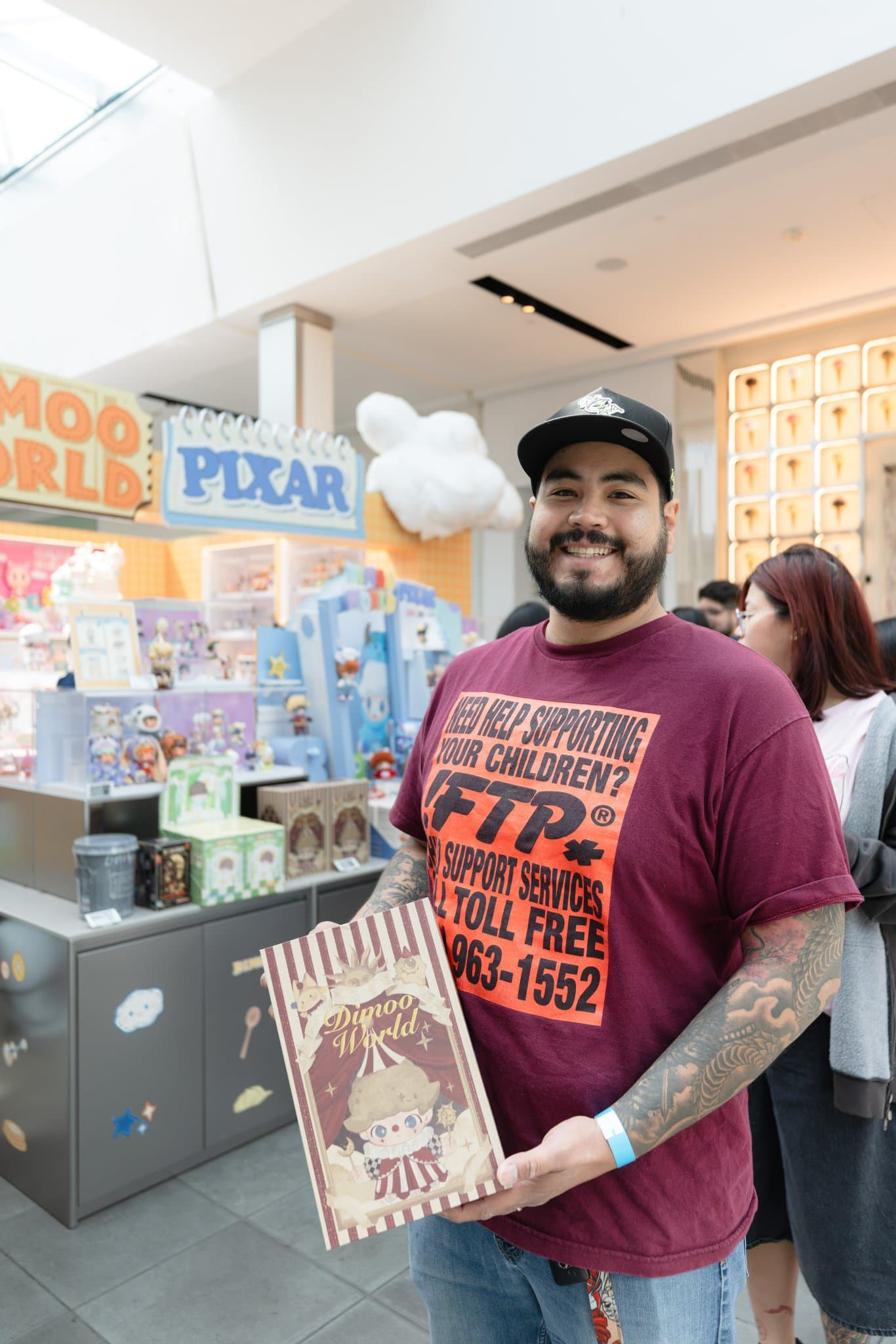 Fan holding a DIMOO WORLD x PIXAR collectible book at the Pop Mart DIMOO WORLD x PIXAR pop-up at Westfield Valley Fair in Santa Clara by JY Studio