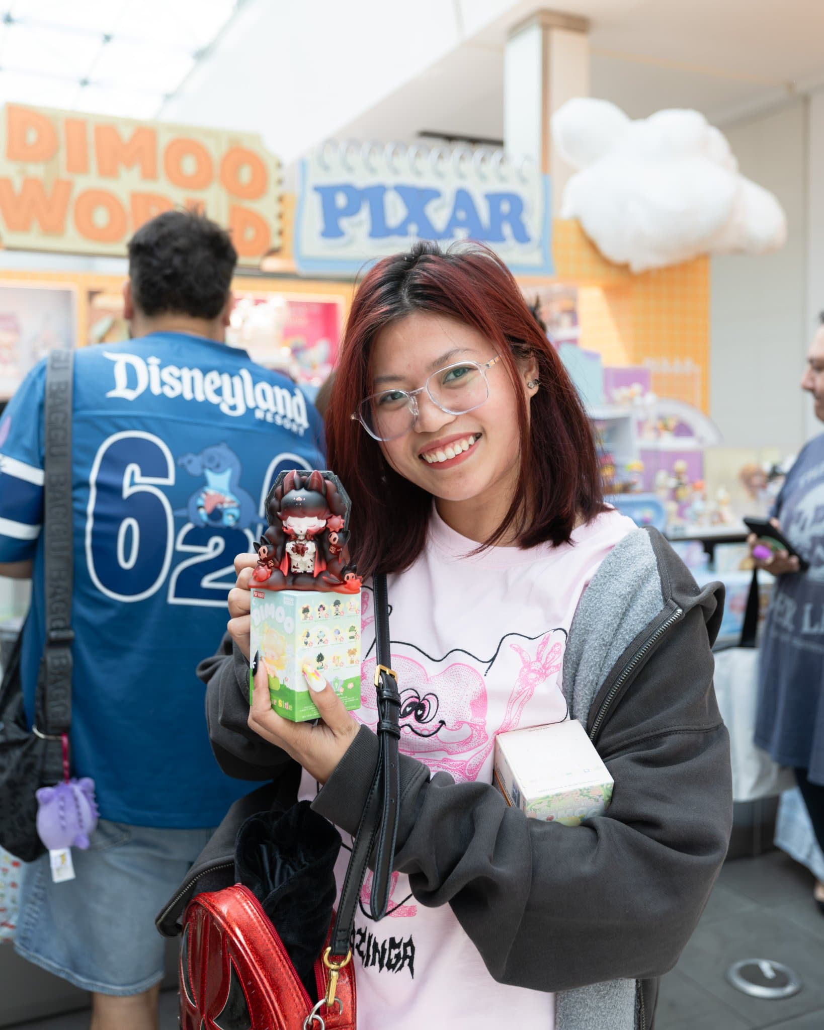 Fan in a Disneyland jersey showing off a DIMOO figure at the Pop Mart DIMOO WORLD x PIXAR pop-up at Westfield Valley Fair in Santa Clara by JY Studio