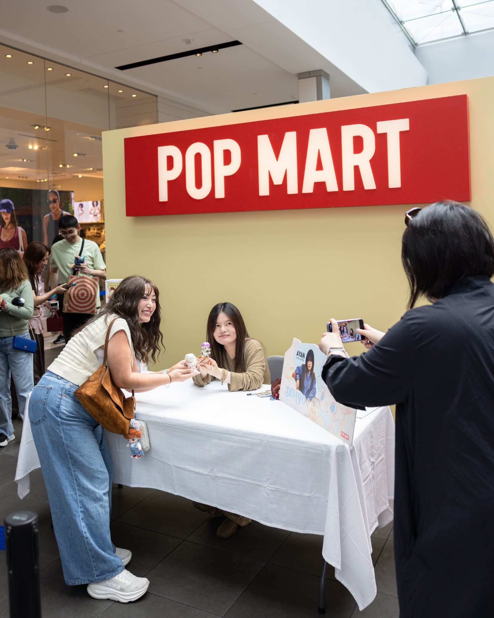 Fans taking photos with DIMOO creator Ayan at the Pop Mart signing table at the Pop Mart DIMOO signing event at Westfield Valley Fair in Santa Clara by JY Studio