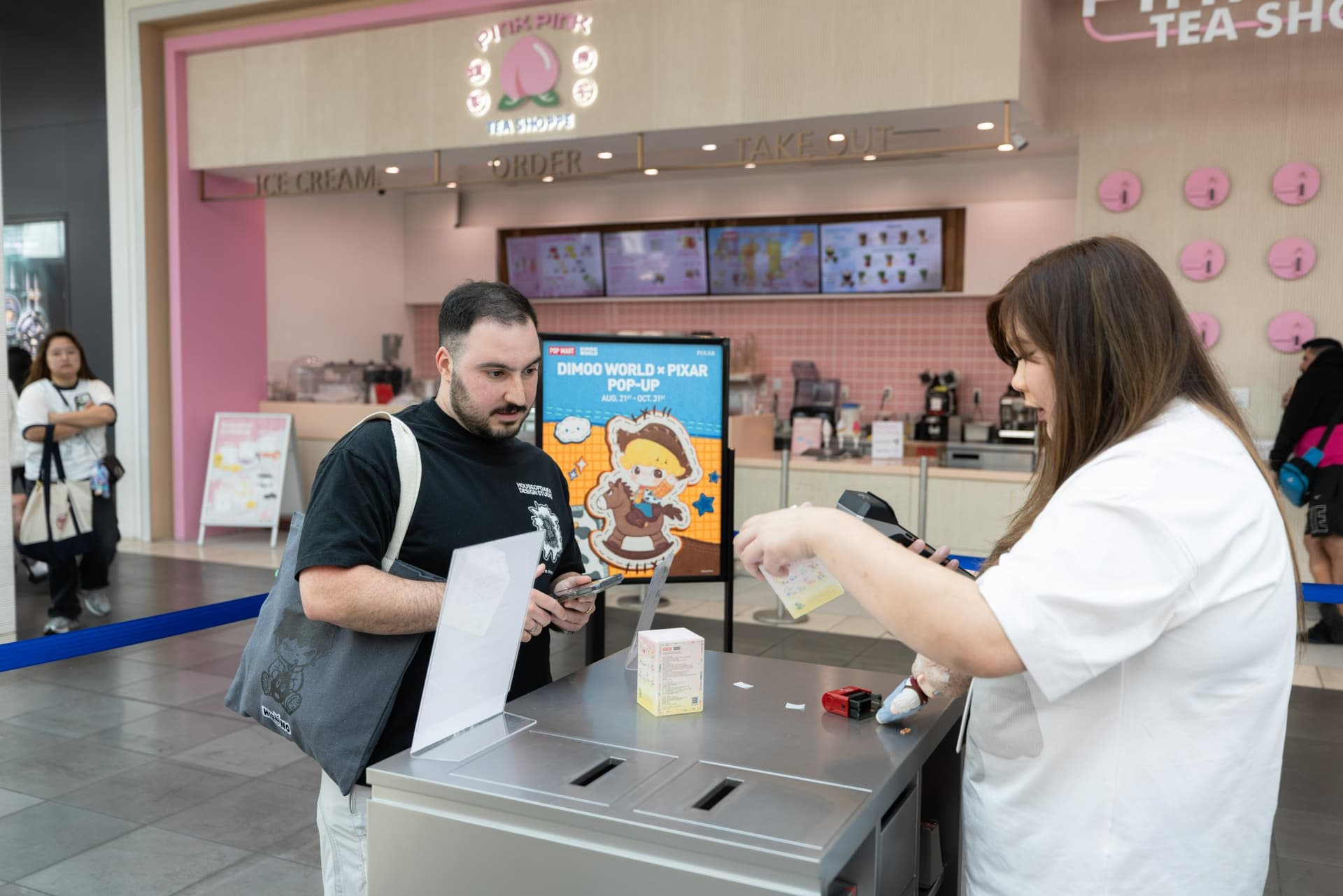 Fan picking up a DIMOO WORLD x PIXAR purchase at the pop-up counter at the Pop Mart DIMOO WORLD x PIXAR pop-up at Westfield Valley Fair in Santa Clara by JY Studio