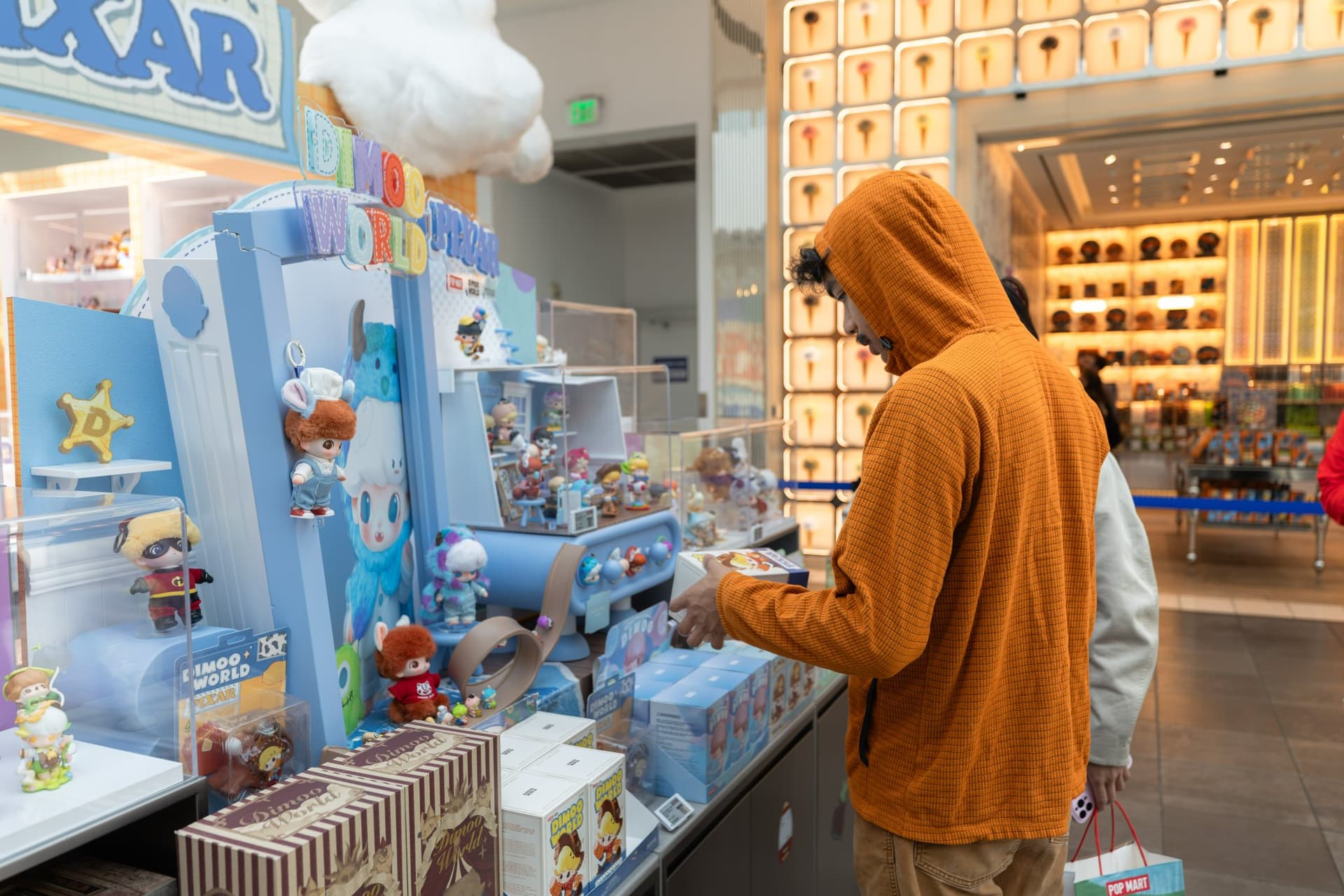 Collector browsing the DIMOO WORLD x PIXAR figure display wall at the Pop Mart DIMOO WORLD x PIXAR pop-up at Westfield Valley Fair in Santa Clara by JY Studio