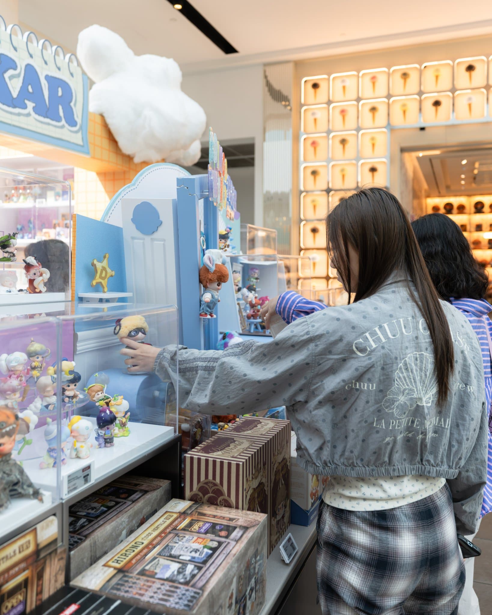 Collector reaching for a DIMOO x PIXAR figure at the display counter at the Pop Mart DIMOO WORLD x PIXAR pop-up at Westfield Valley Fair in Santa Clara by JY Studio