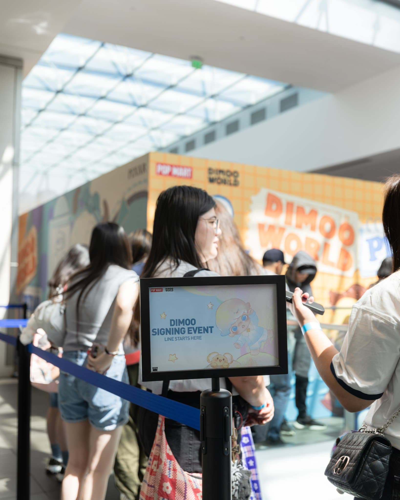 "DIMOO Signing Event — Line Starts Here" sign with fans queuing at the Pop Mart DIMOO signing event at Westfield Valley Fair in Santa Clara by JY Studio