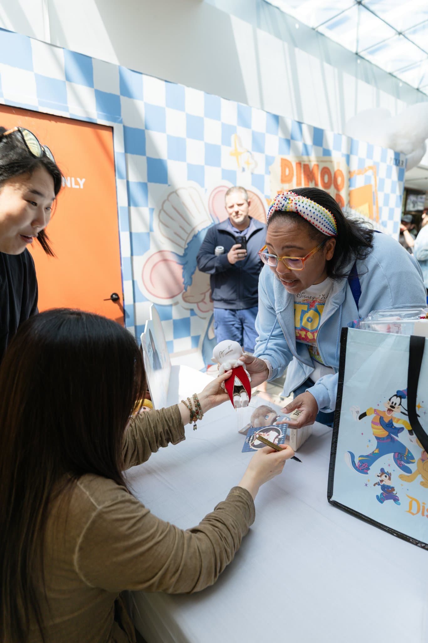 Excited fan showing a DIMOO figure to creator Ayan at the signing table at the Pop Mart DIMOO signing event at Westfield Valley Fair in Santa Clara by JY Studio