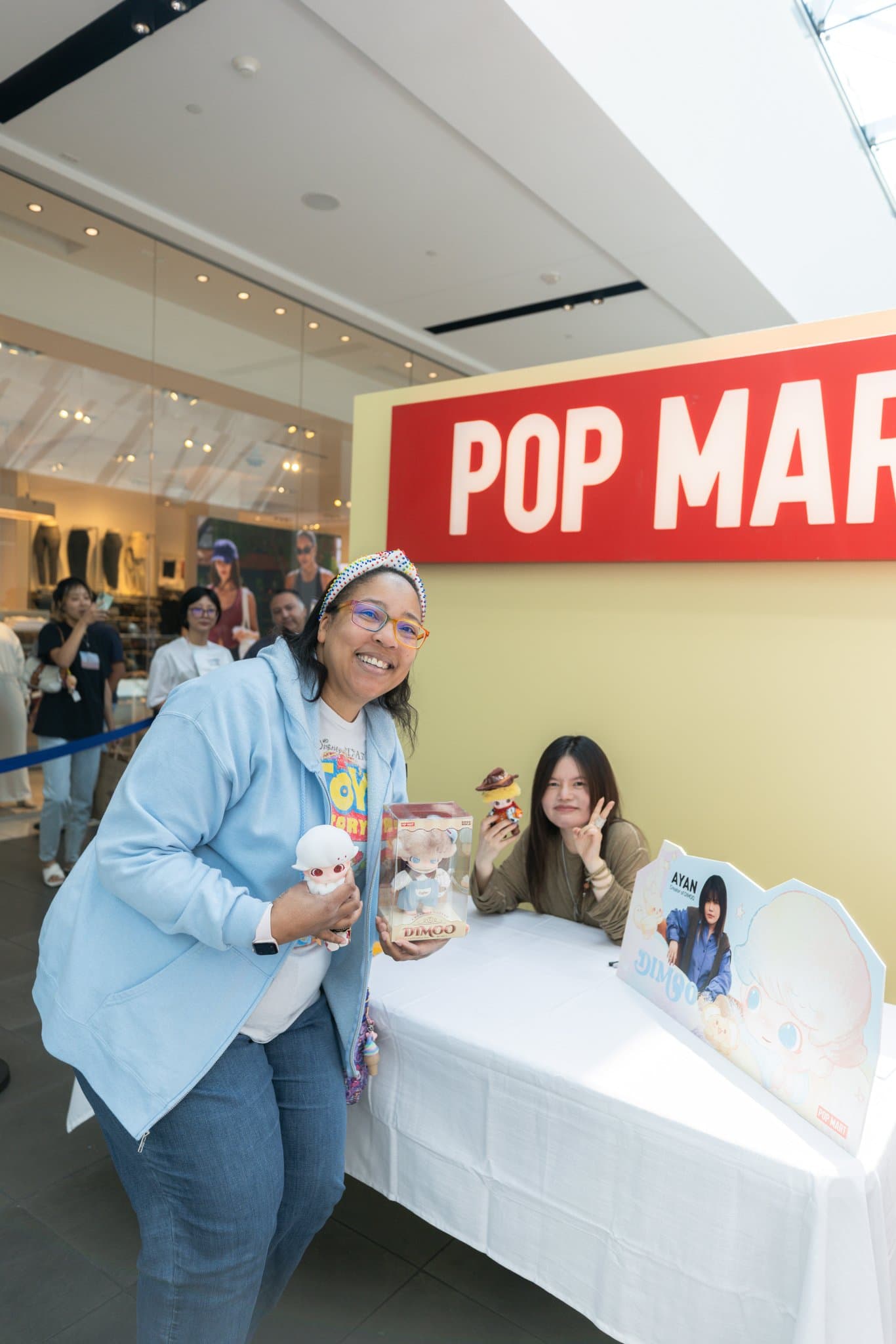 Fan posing with DIMOO creator Ayan under the Pop Mart sign at the Pop Mart DIMOO signing event at Westfield Valley Fair in Santa Clara by JY Studio