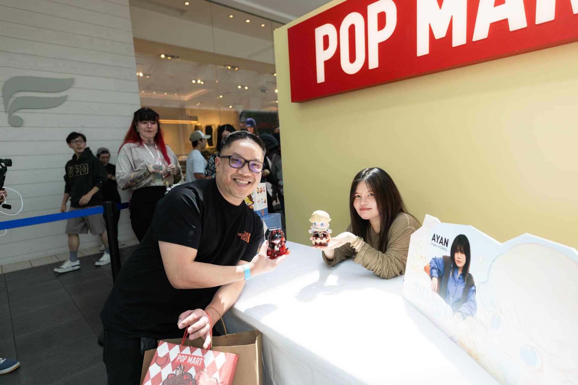 Fan posing behind the signing table with DIMOO artist Ayan at the Pop Mart DIMOO signing event at Westfield Valley Fair in Santa Clara by JY Studio
