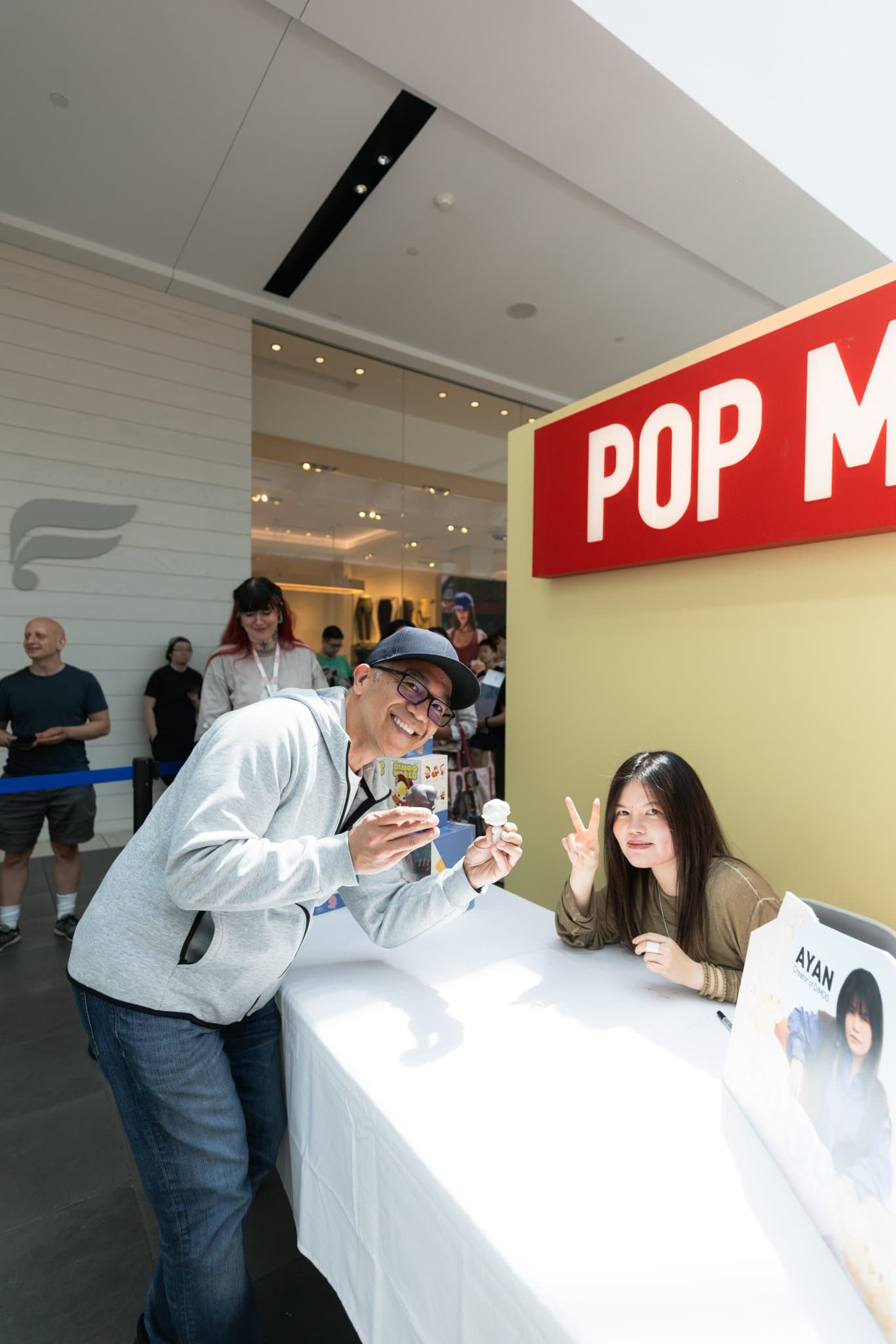 Fan making a peace sign with DIMOO creator Ayan at the Pop Mart table at the Pop Mart DIMOO signing event at Westfield Valley Fair in Santa Clara by JY Studio