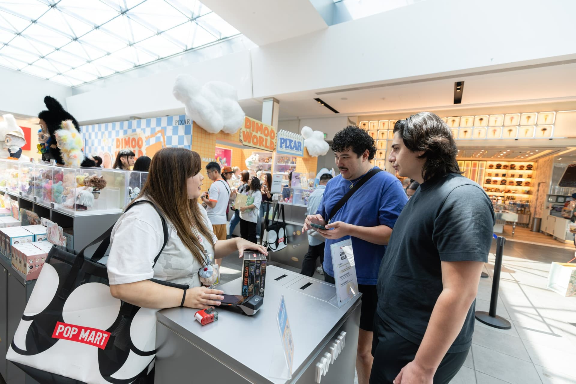 Shoppers at the DIMOO pop-up checkout with a Pop Mart tote bag at the Pop Mart DIMOO WORLD x PIXAR pop-up at Westfield Valley Fair in Santa Clara by JY Studio