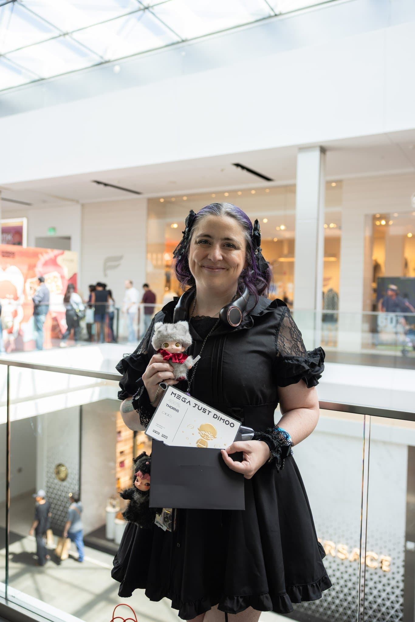 Fan in a black dress holding a DIMOO figure and signed card at the Pop Mart DIMOO signing event at Westfield Valley Fair in Santa Clara by JY Studio