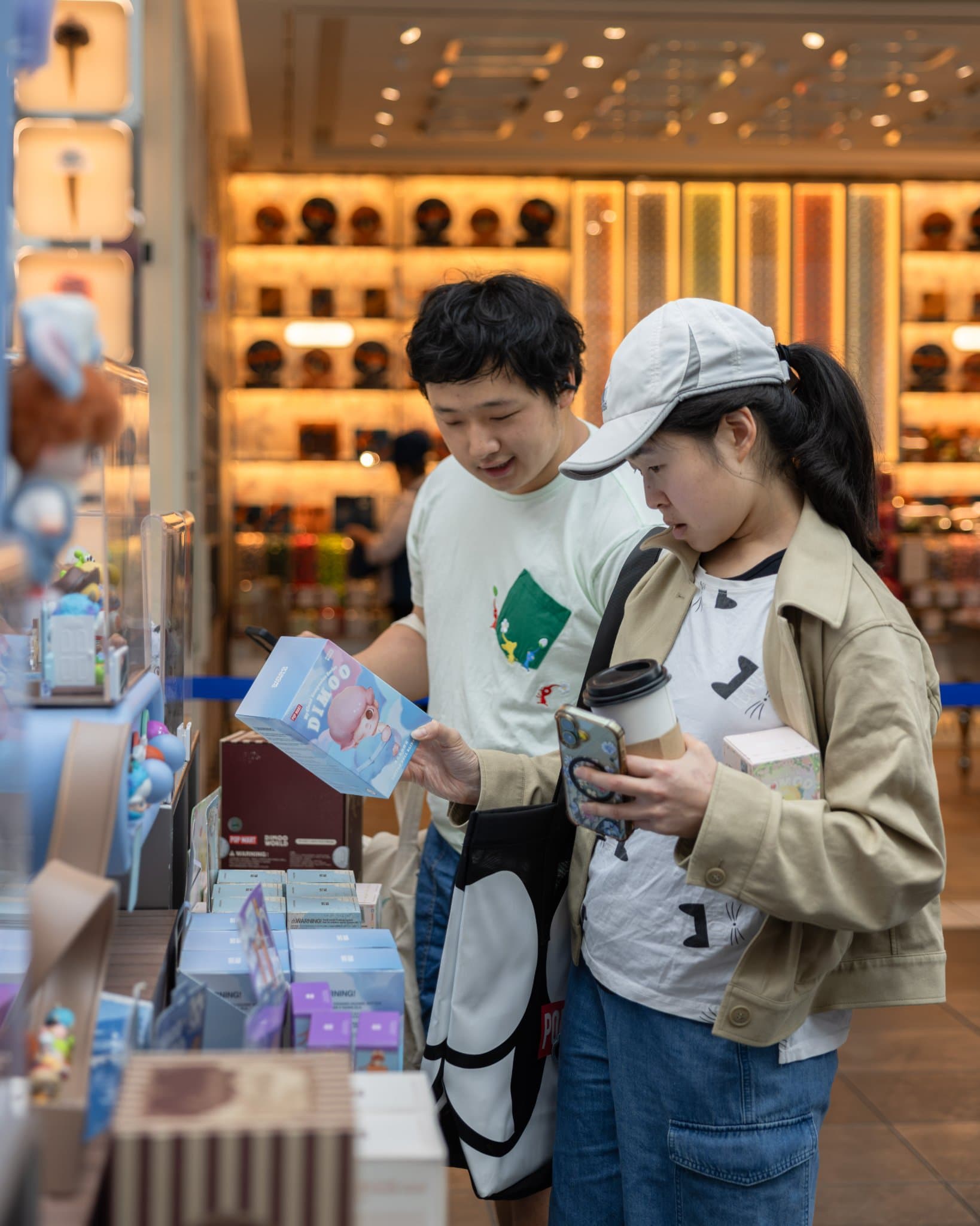 Two friends looking at a DIMOO blind box at the pop-up at the Pop Mart DIMOO WORLD x PIXAR pop-up at Westfield Valley Fair in Santa Clara by JY Studio