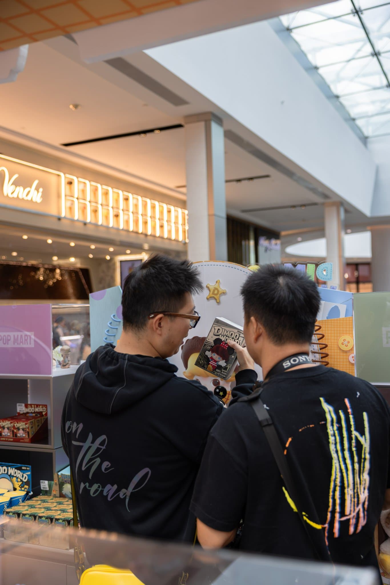 Two collectors comparing a DIMOO figure at the pop-up at the Pop Mart DIMOO WORLD x PIXAR pop-up at Westfield Valley Fair in Santa Clara by JY Studio