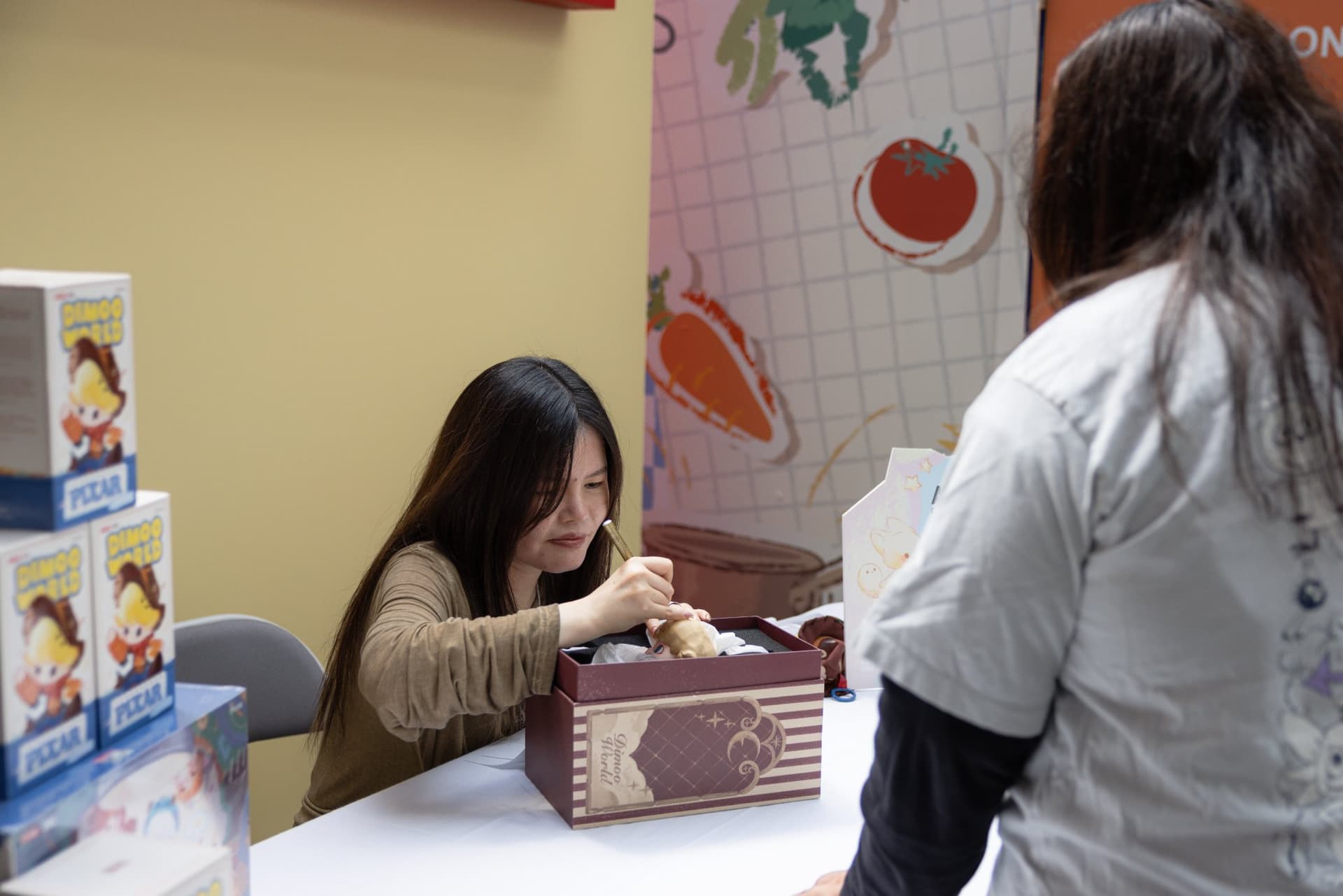 DIMOO creator Ayan signing a DIMOO collectible box at the Pop Mart DIMOO signing event at Westfield Valley Fair in Santa Clara by JY Studio
