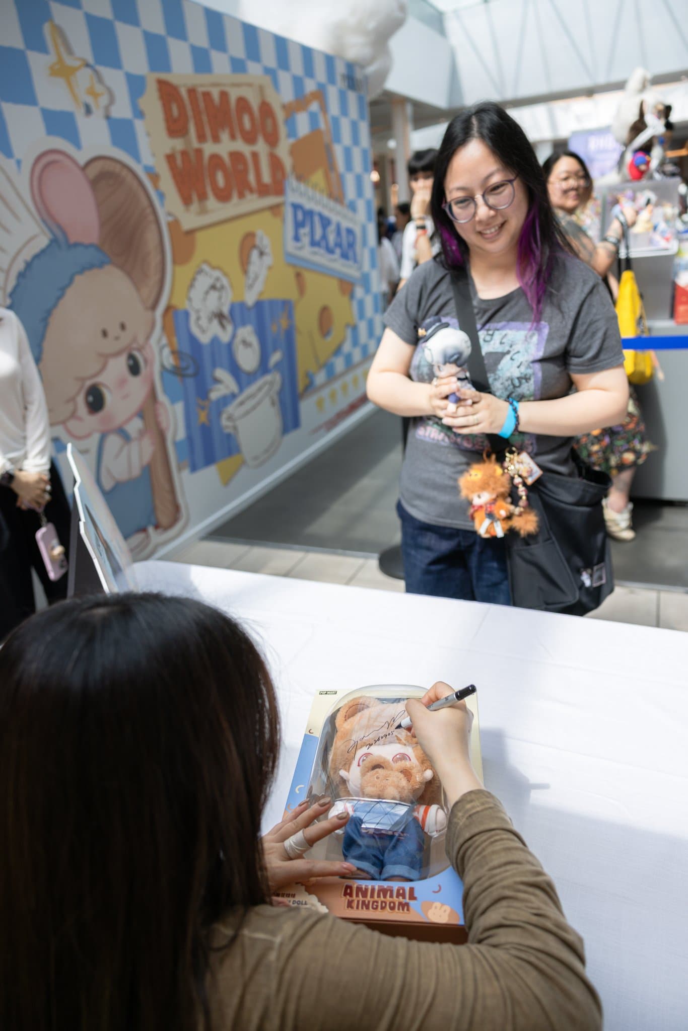 DIMOO creator Ayan signing a boxed DIMOO Animal Kingdom figure as a fan watches at the Pop Mart DIMOO signing event at Westfield Valley Fair in Santa Clara by JY Studio