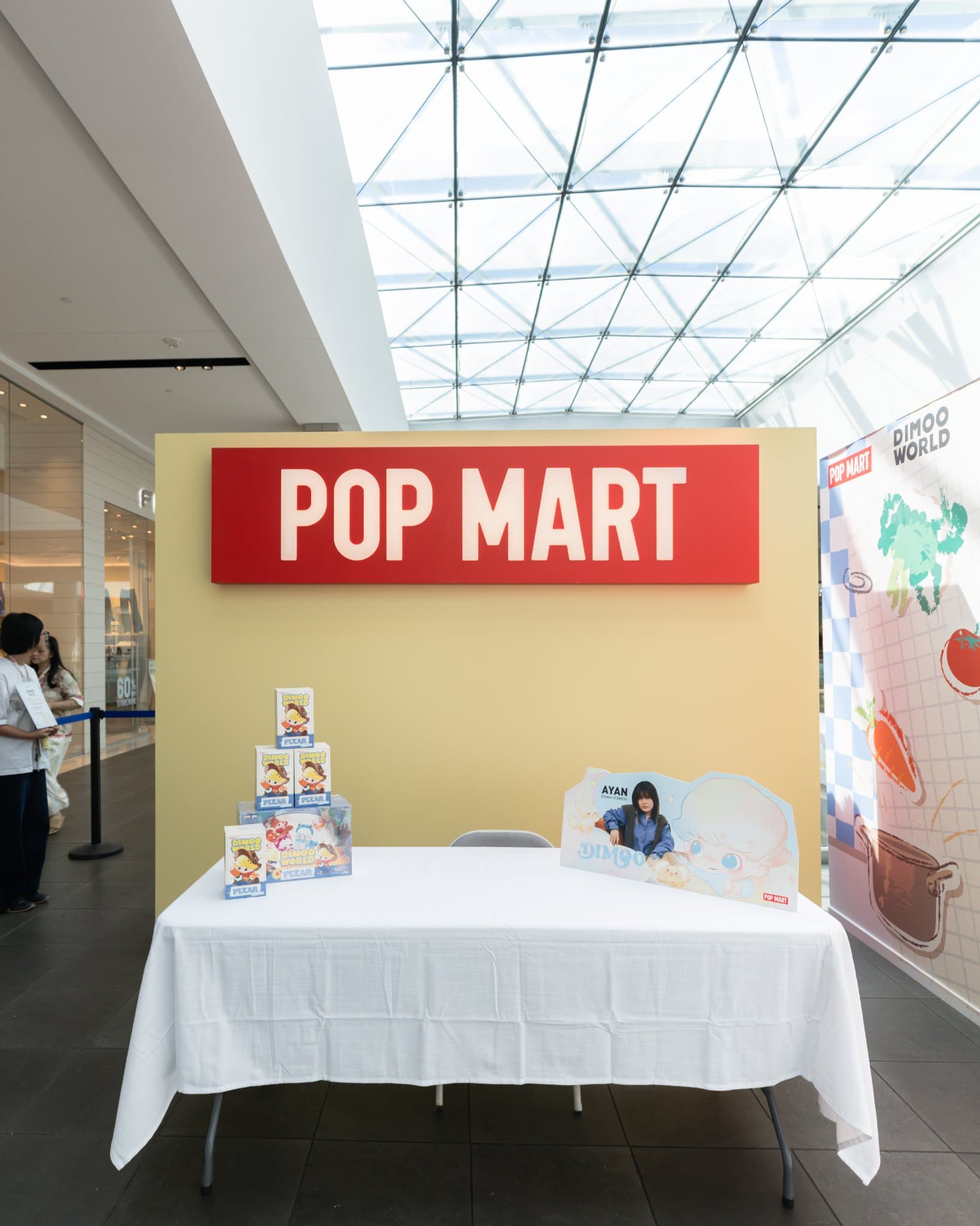 Pop Mart DIMOO signing table set up with DIMOO WORLD x PIXAR boxes and Ayan name card at the Pop Mart DIMOO signing event at Westfield Valley Fair in Santa Clara by JY Studio