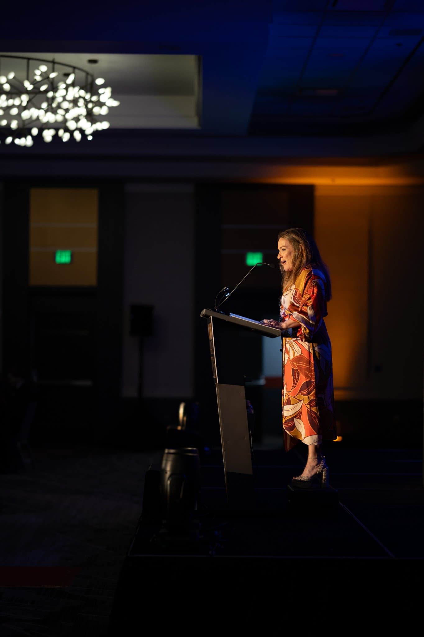 Speaker at the podium beneath the ballroom chandelier with warm amber uplighting at Admin Awards 2026 at SFO Marriott Waterfront, Burlingame by JY Studio