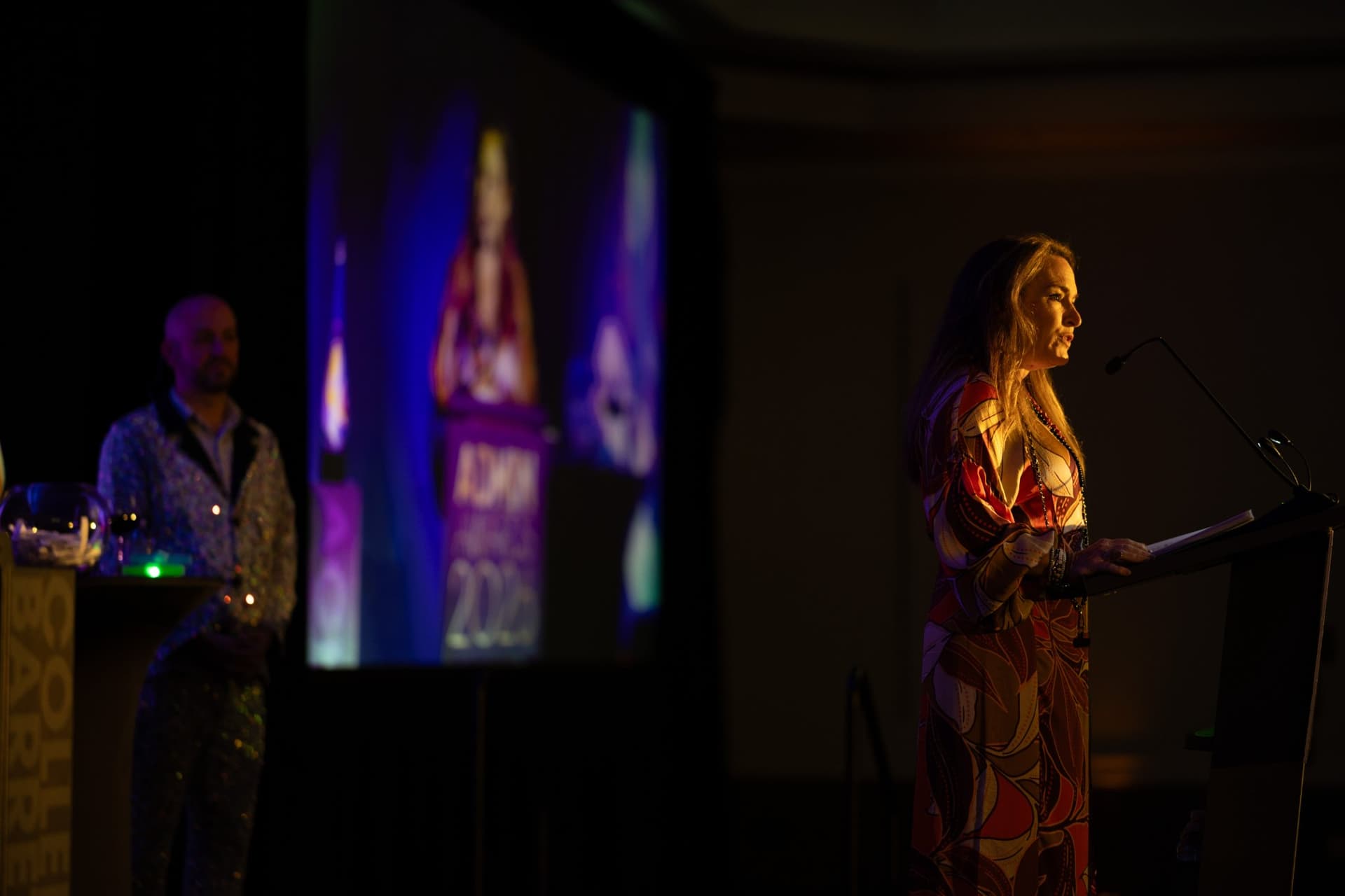 Speaker at the podium with the emcee and stage screen in the background at Admin Awards 2026 at SFO Marriott Waterfront, Burlingame by JY Studio