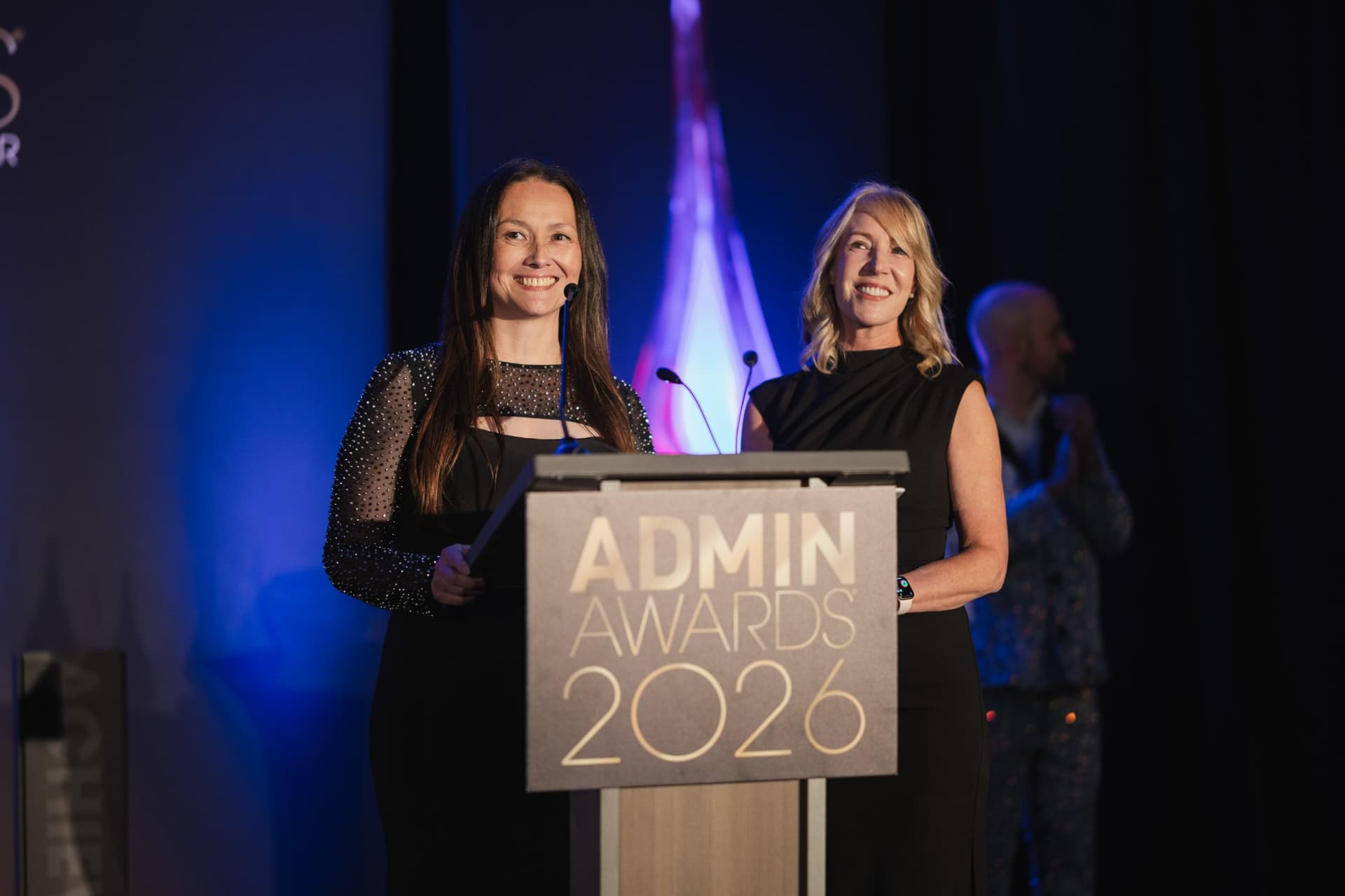 Two honorees smiling together at the Admin Awards 2026 podium at Admin Awards 2026 at SFO Marriott Waterfront, Burlingame by JY Studio