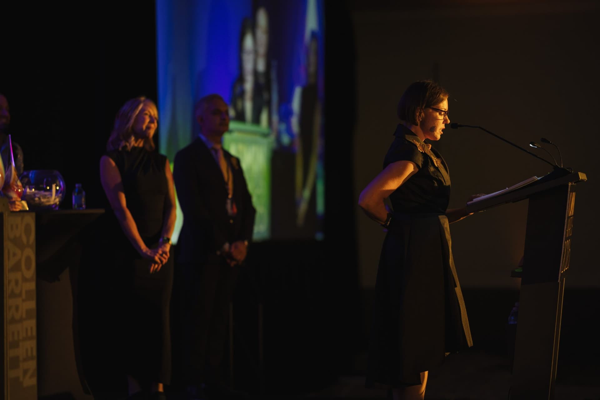 Honoree speaking at the lectern while presenters stand by on stage at Admin Awards 2026 at SFO Marriott Waterfront, Burlingame by JY Studio