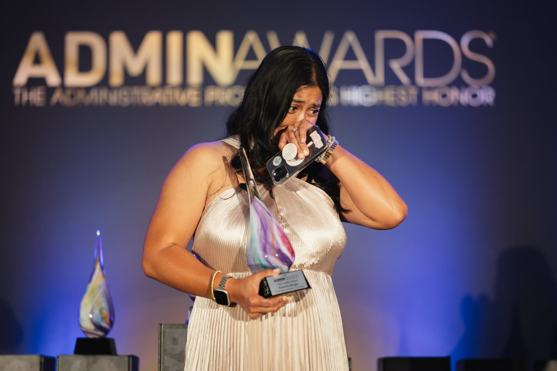 Emotional award winner wiping away tears while holding her trophy on stage at Admin Awards 2026 at SFO Marriott Waterfront, Burlingame by JY Studio