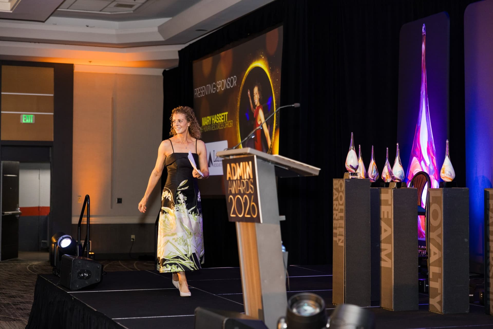 Speaker walking onto the stage past the presenting sponsor screen and award pillars at Admin Awards 2026 at SFO Marriott Waterfront, Burlingame by JY Studio