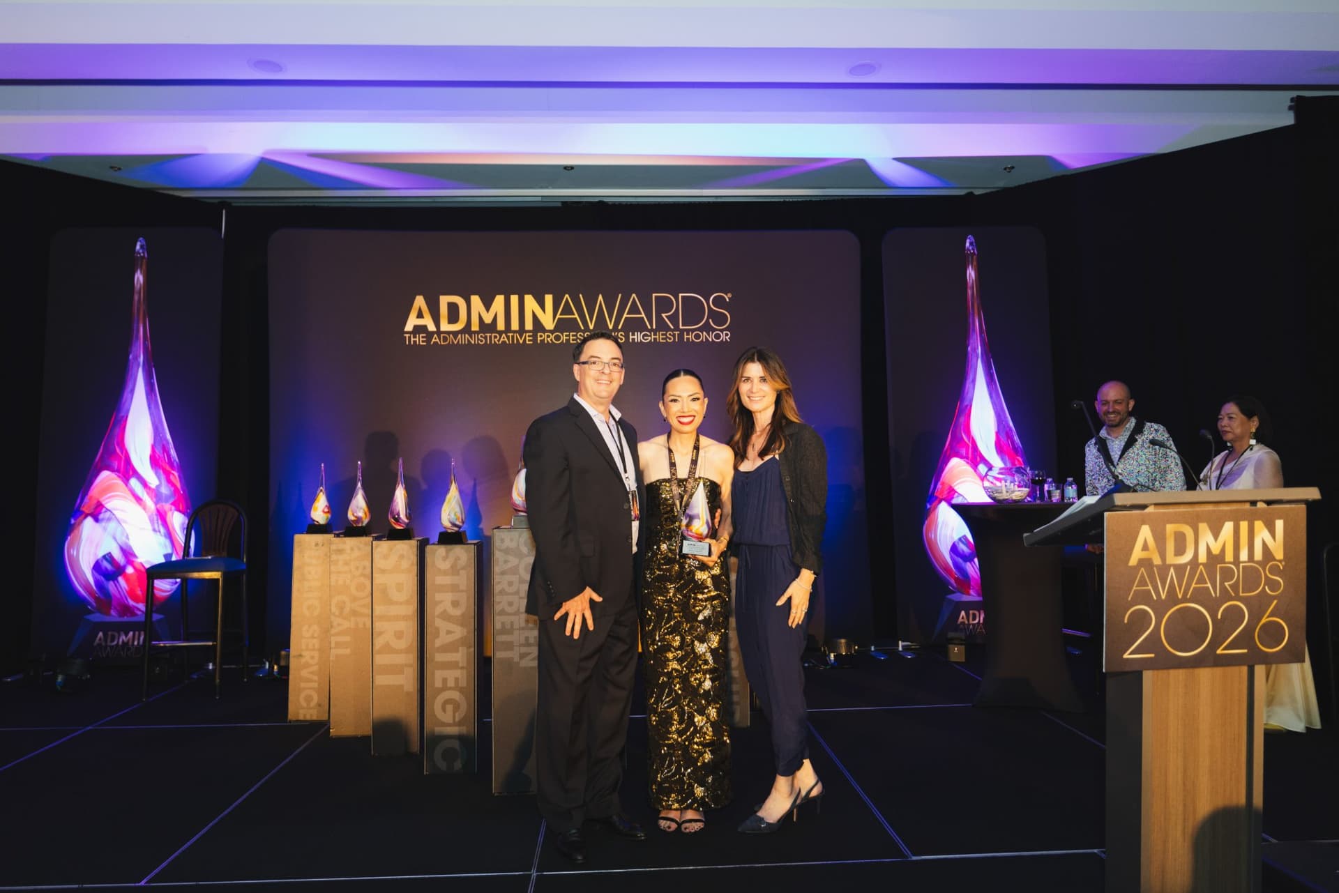 Award winner posing with her trophy and presenters on stage at Admin Awards 2026 at SFO Marriott Waterfront, Burlingame by JY Studio