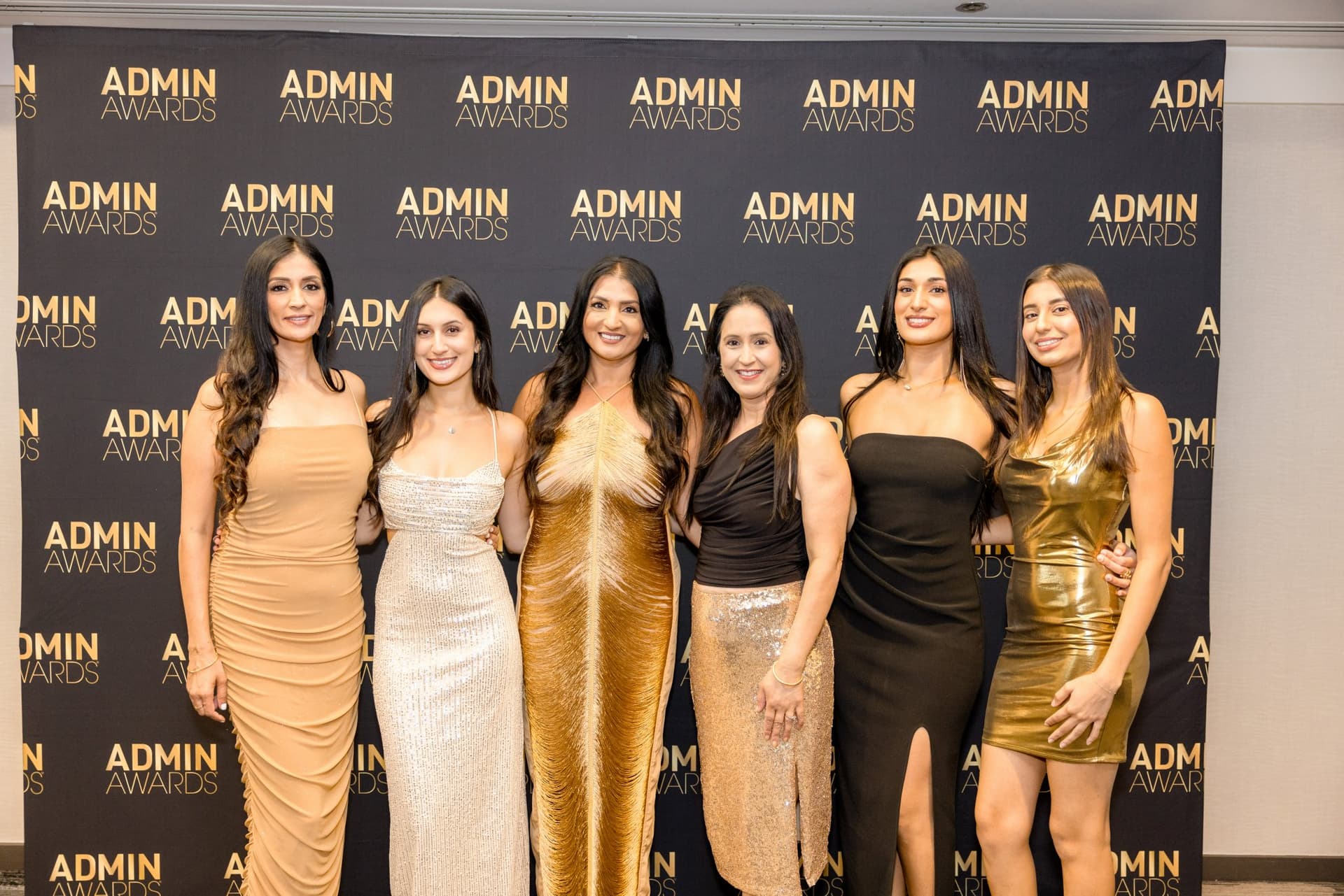Six guests in gold and black gowns posing at the Admin Awards step-and-repeat at Admin Awards 2026 at SFO Marriott Waterfront, Burlingame by JY Studio