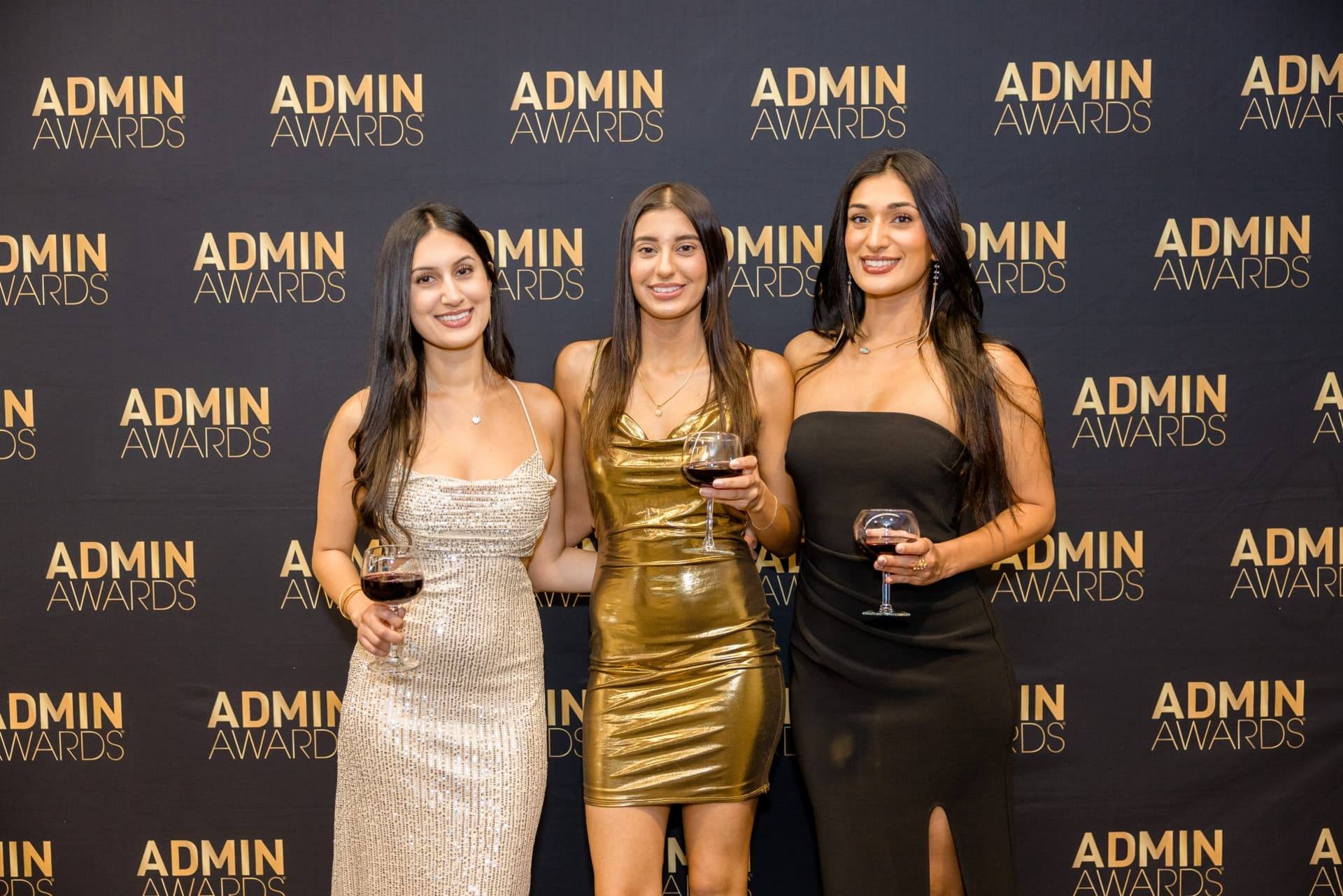 Three guests with wine glasses posing at the Admin Awards step-and-repeat at Admin Awards 2026 at SFO Marriott Waterfront, Burlingame by JY Studio
