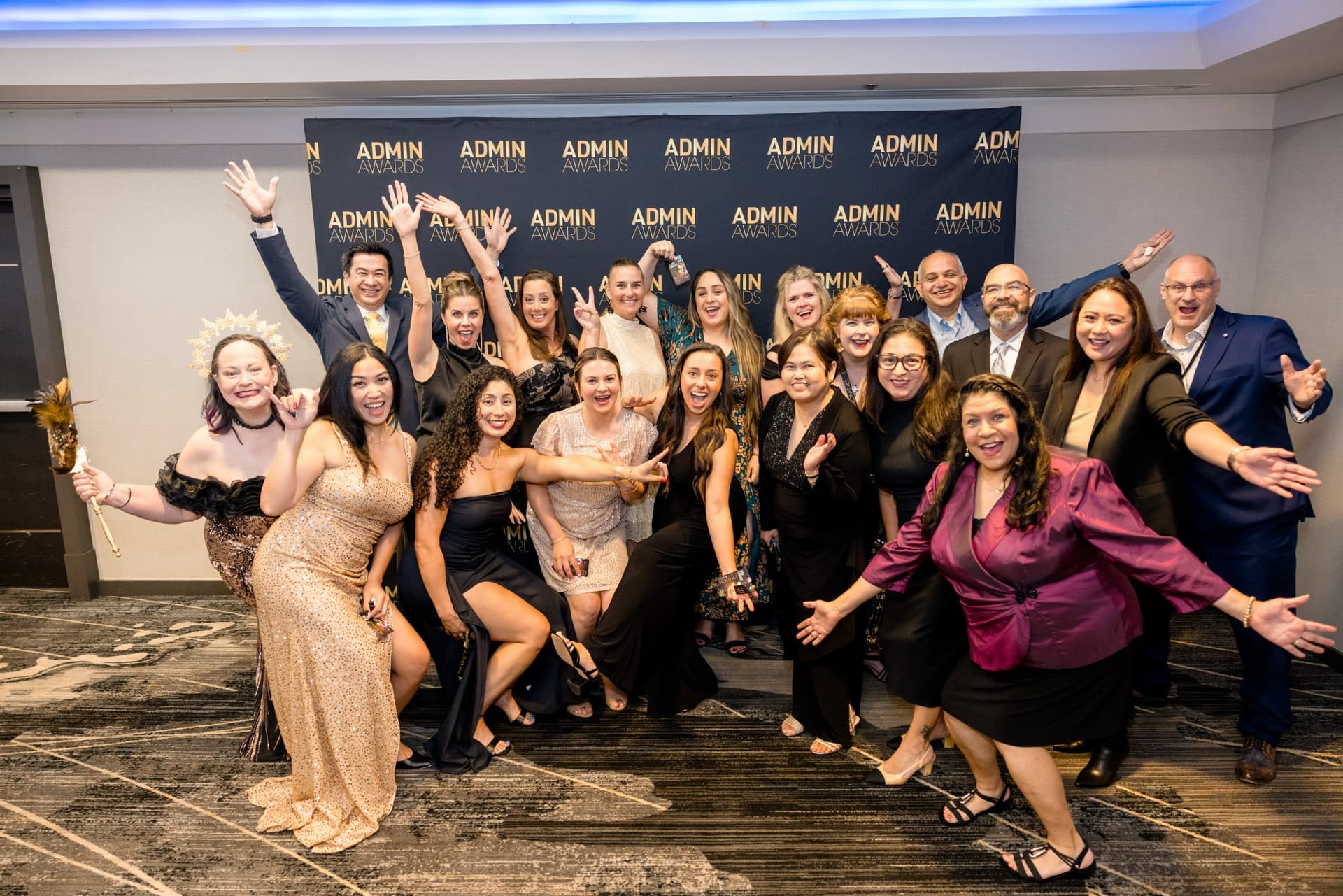 Group of guests cheering with arms outstretched in front of the step-and-repeat at Admin Awards 2026 at SFO Marriott Waterfront, Burlingame by JY Studio