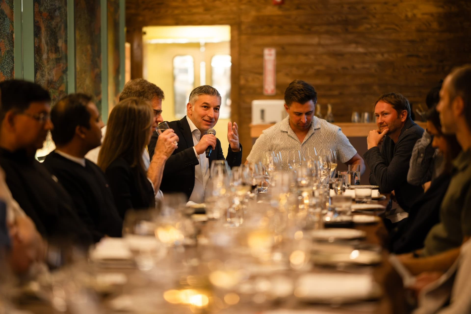 Executive speaking with a microphone at the end of the long table at the Business Insider AI Insider executive dinner The Great Coding Reset during SF Tech Week 2026 in San Francisco by JY Studio