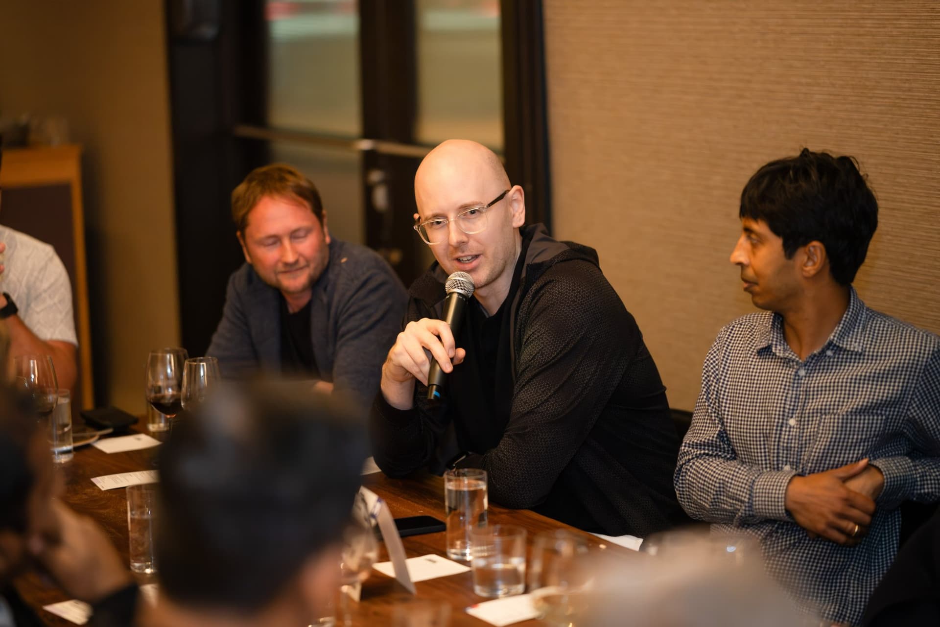 AI Insider host speaking with a microphone from his seat at the table at the Business Insider AI Insider executive dinner The Great Coding Reset during SF Tech Week 2026 in San Francisco by JY Studio