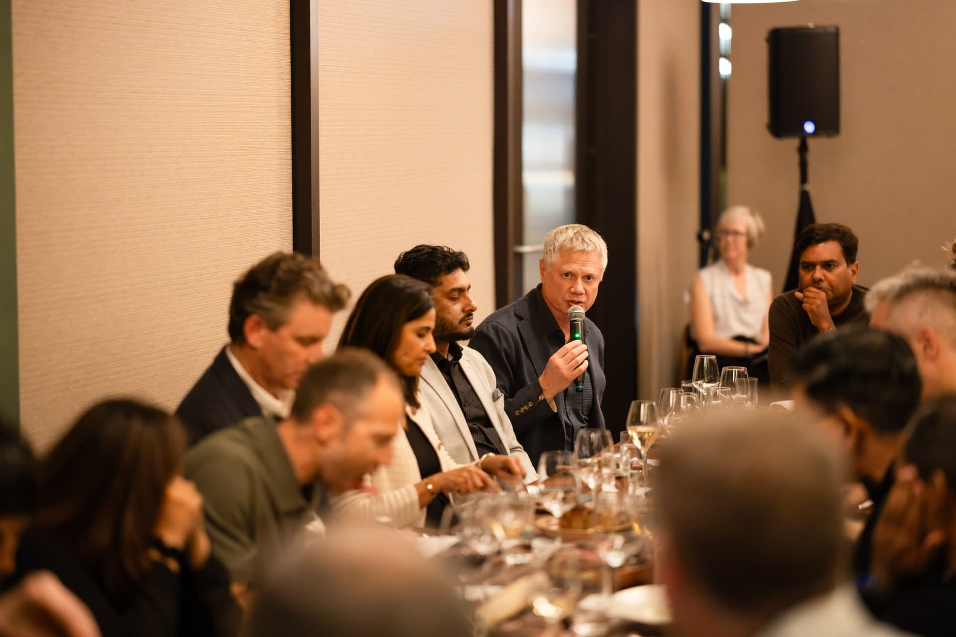 Executive in a navy blazer speaking with a microphone at the Business Insider AI Insider executive dinner The Great Coding Reset during SF Tech Week 2026 in San Francisco by JY Studio