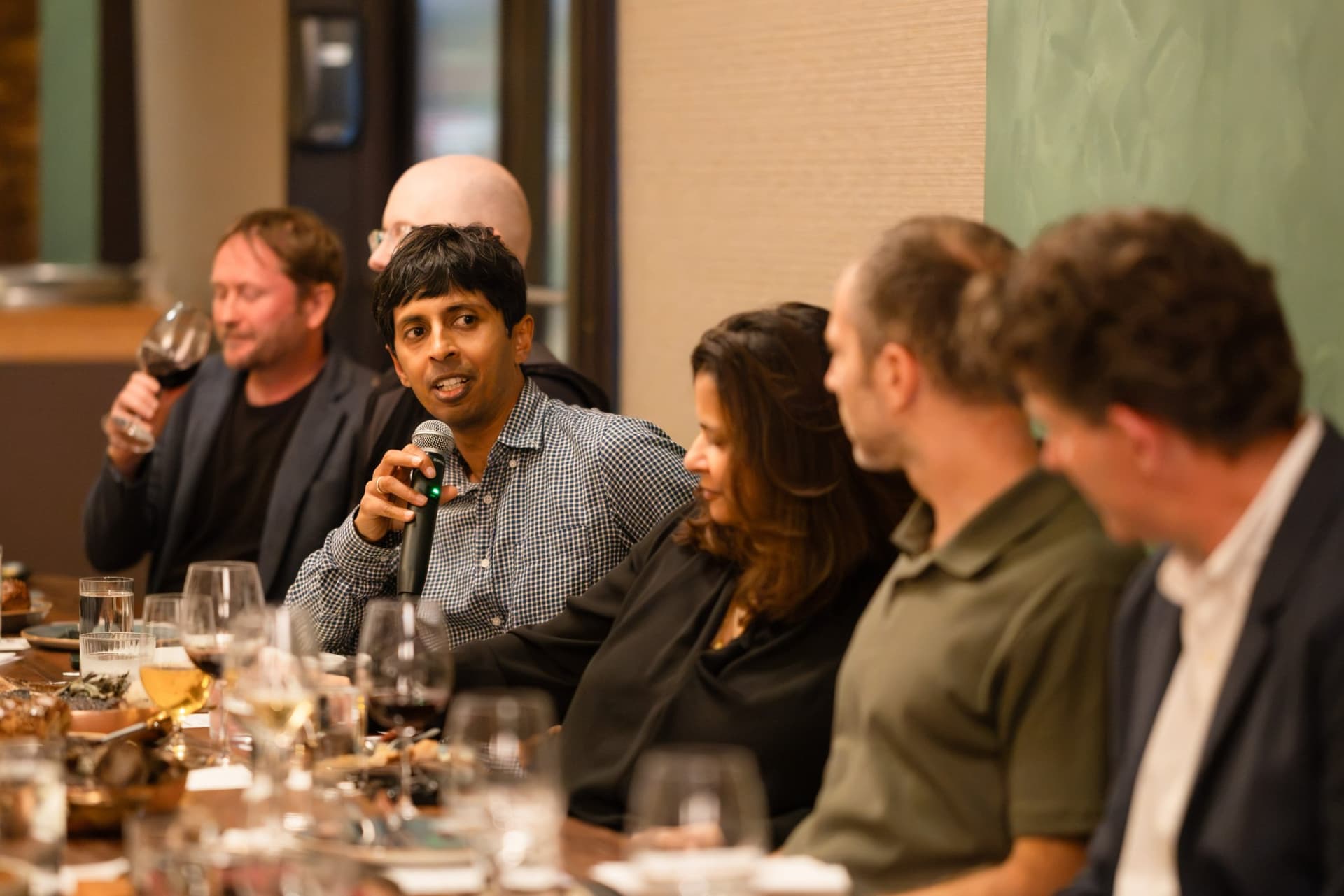 Executive holding a glass of wine while speaking with a microphone at the Business Insider AI Insider executive dinner The Great Coding Reset during SF Tech Week 2026 in San Francisco by JY Studio