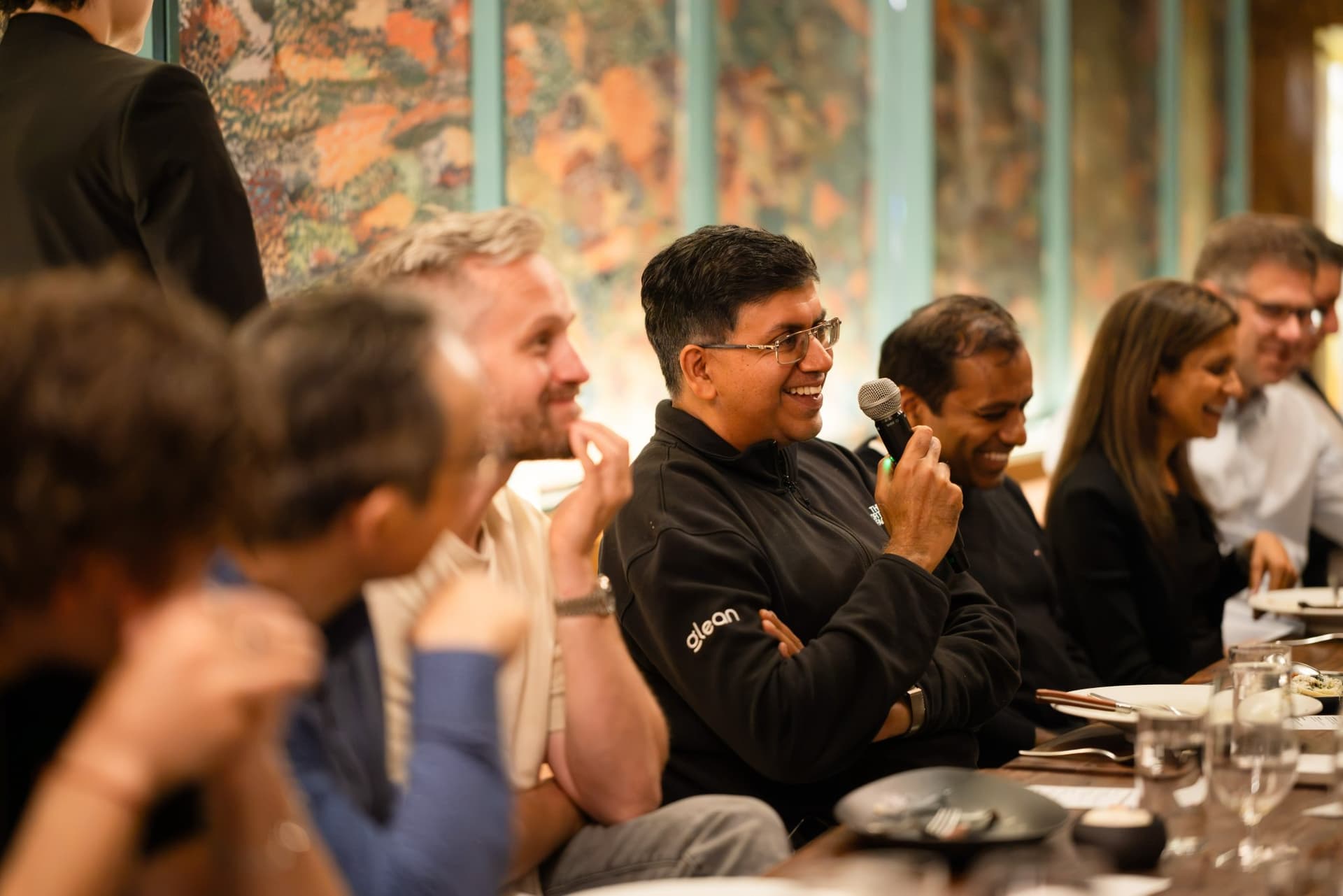 Executive in a Glean jacket laughing with a microphone during the roundtable at the Business Insider AI Insider executive dinner The Great Coding Reset during SF Tech Week 2026 in San Francisco by JY Studio