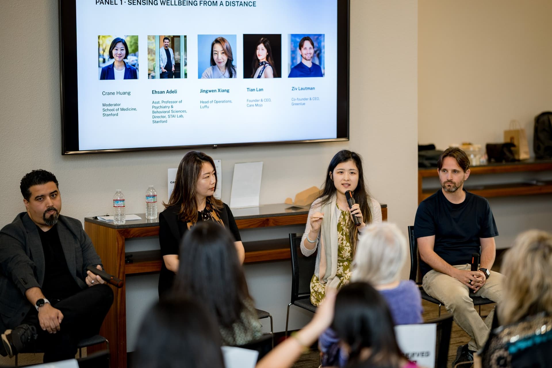 Moderator and panelists of Panel 1 "Sensing Wellbeing from a Distance" seated beneath the panel title slide at Care at a Distance: AI, Sensors, Robotics and the Future of Aging, SF Tech Week 2026 at EVGR, Stanford University by JY Studio