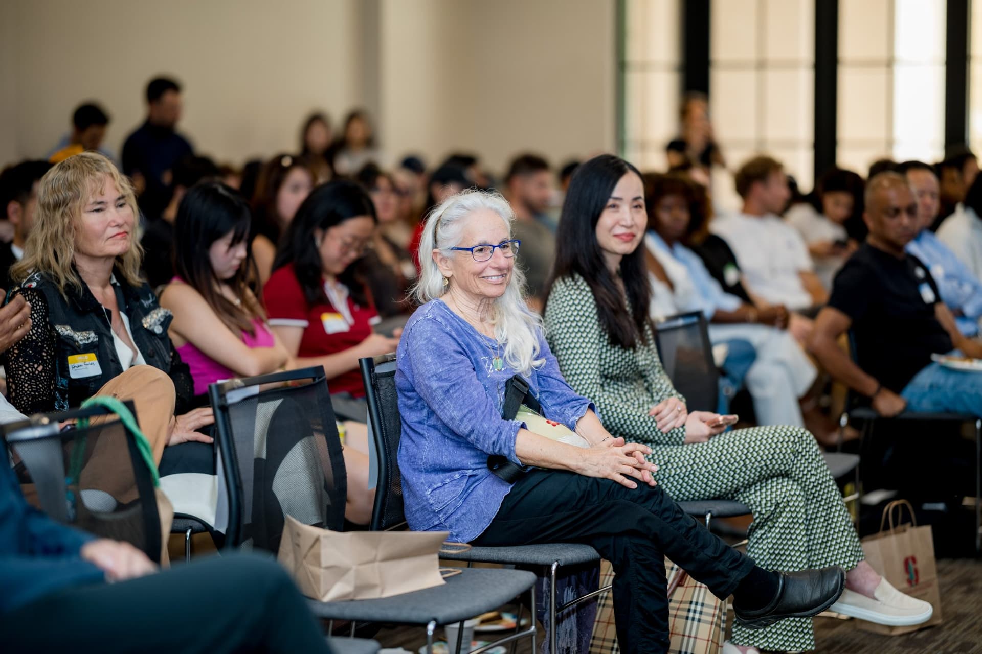 Smiling attendees in the front rows listening to the conversation on aging and technology at Care at a Distance: AI, Sensors, Robotics and the Future of Aging, SF Tech Week 2026 at EVGR, Stanford University by JY Studio
