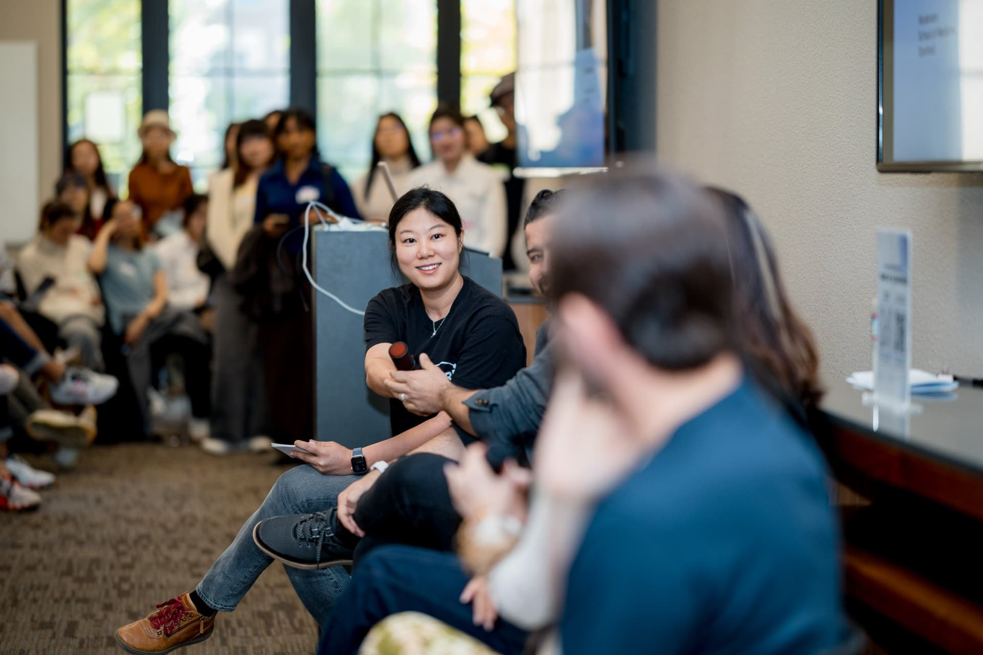 Event host in a Care at a Distance T-shirt smiling at the audience during the panel at Care at a Distance: AI, Sensors, Robotics and the Future of Aging, SF Tech Week 2026 at EVGR, Stanford University by JY Studio