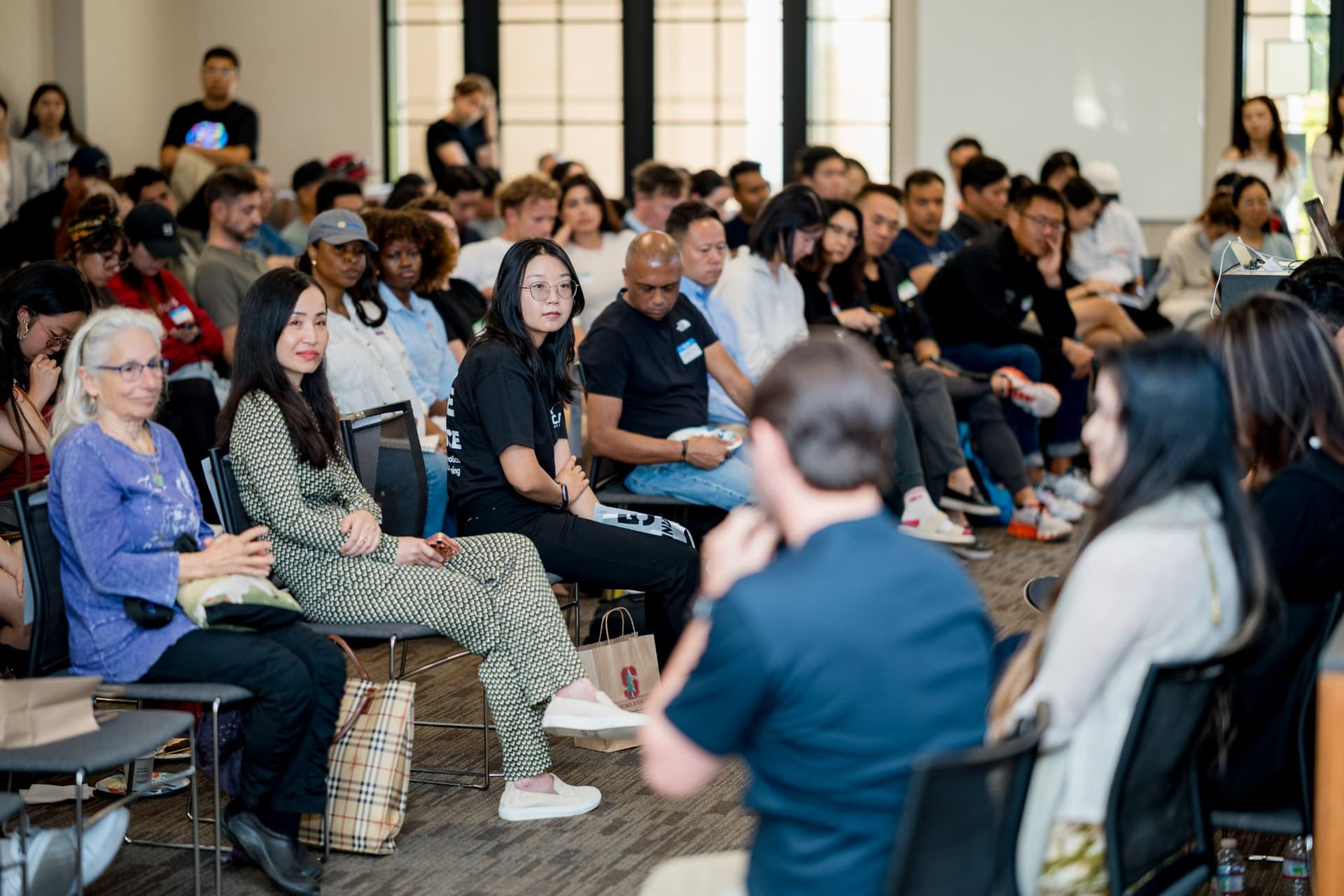 Audience members turning toward a speaker during the open Q&A at Care at a Distance: AI, Sensors, Robotics and the Future of Aging, SF Tech Week 2026 at EVGR, Stanford University by JY Studio