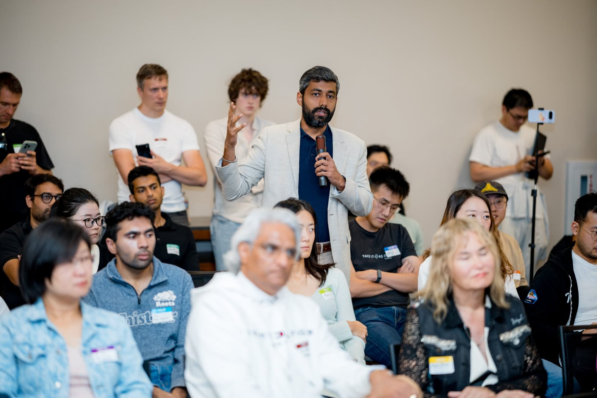Attendee standing in the crowd to ask the panel a question with a microphone at Care at a Distance: AI, Sensors, Robotics and the Future of Aging, SF Tech Week 2026 at EVGR, Stanford University by JY Studio