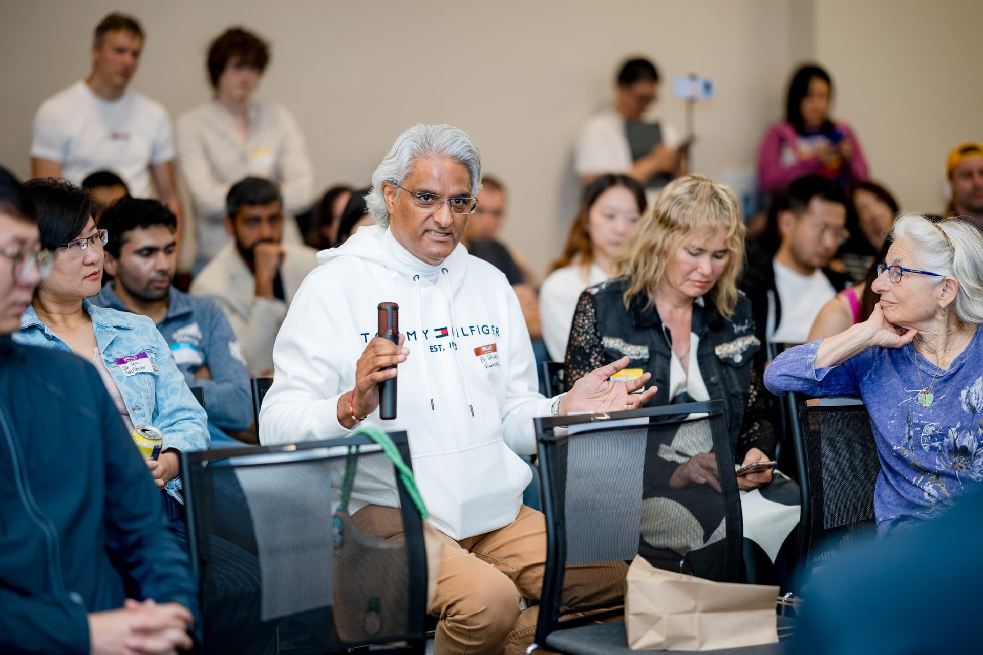 Attendee in a white hoodie asking the panel a question during audience Q&A at Care at a Distance: AI, Sensors, Robotics and the Future of Aging, SF Tech Week 2026 at EVGR, Stanford University by JY Studio