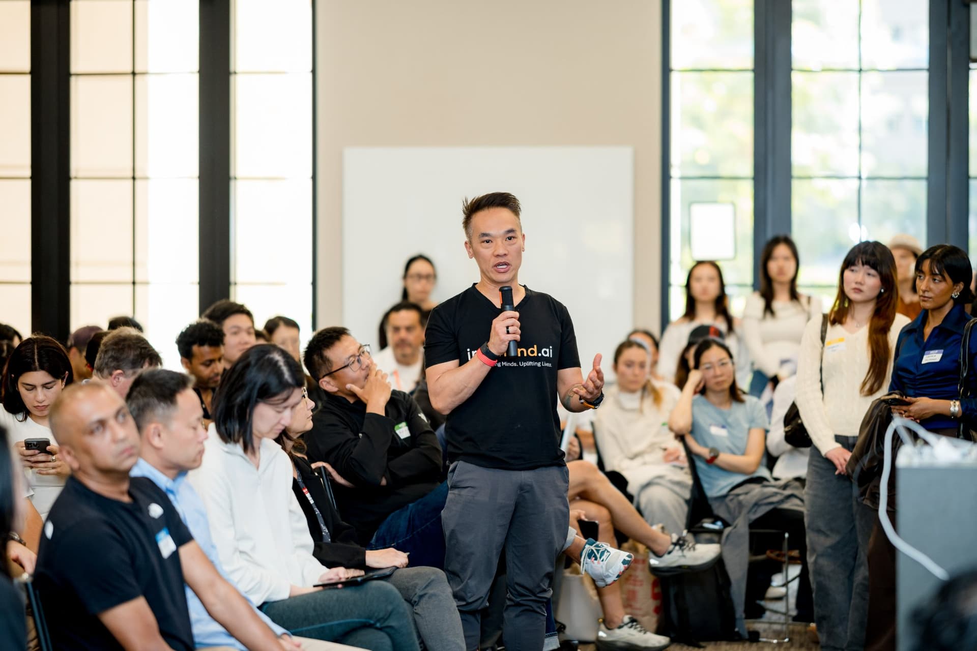Founder standing in the middle of the audience to ask a question with a microphone at Care at a Distance: AI, Sensors, Robotics and the Future of Aging, SF Tech Week 2026 at EVGR, Stanford University by JY Studio