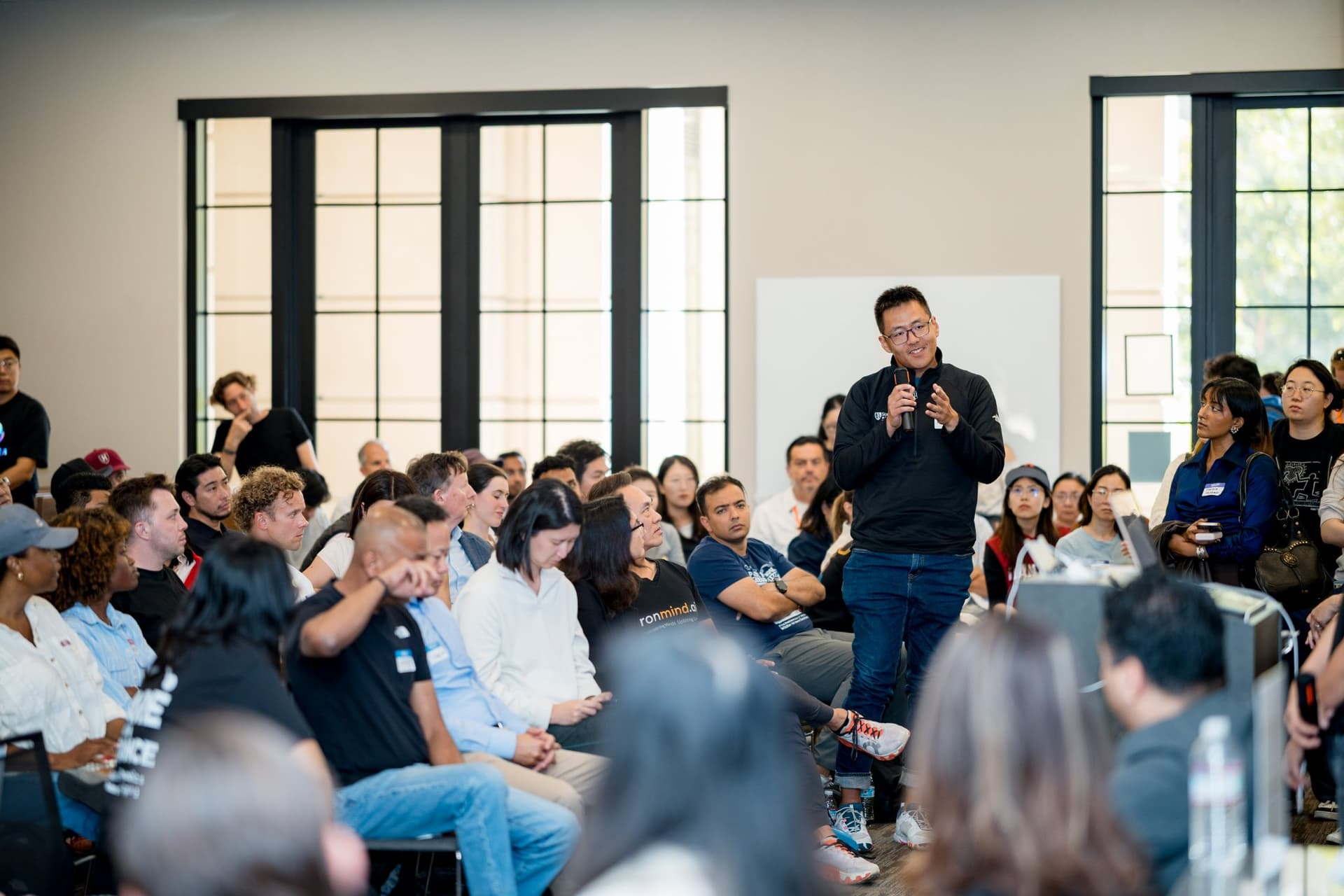 Attendee standing to ask a question in a packed room of founders and researchers at Care at a Distance: AI, Sensors, Robotics and the Future of Aging, SF Tech Week 2026 at EVGR, Stanford University by JY Studio