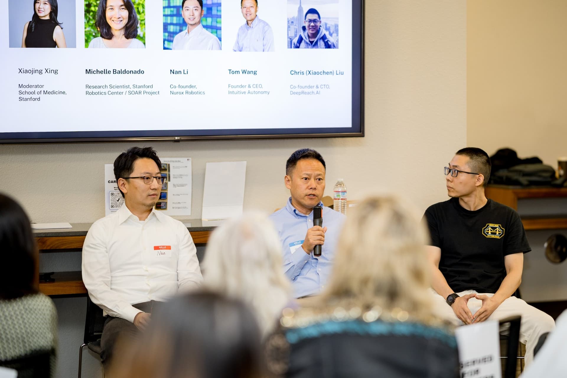 Three panelists of Panel 2 "Robotics for Independent Living" seated in front of the speaker slide at Care at a Distance: AI, Sensors, Robotics and the Future of Aging, SF Tech Week 2026 at EVGR, Stanford University by JY Studio