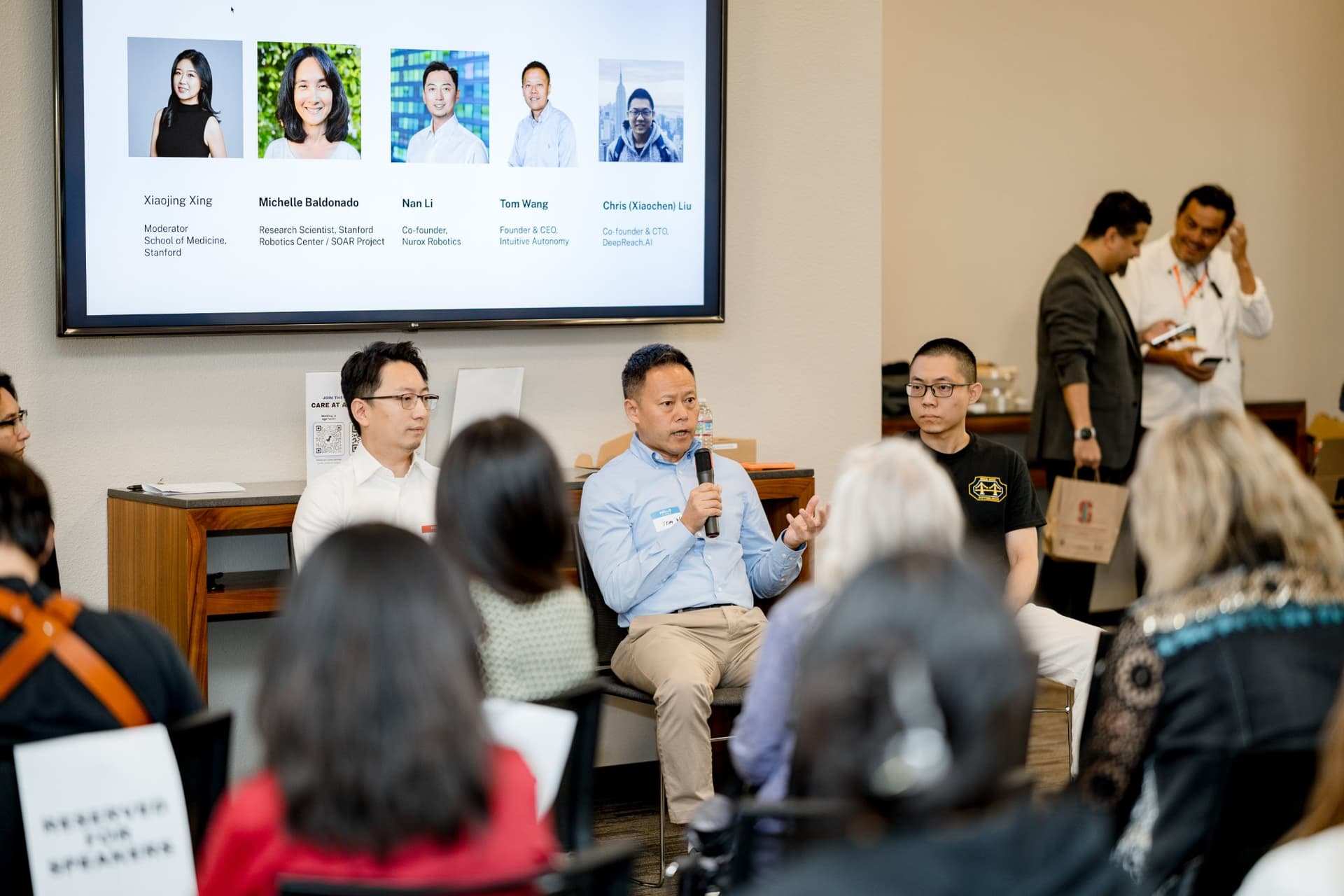Panelist in a light blue shirt answering a question during Panel 2 "Robotics for Independent Living" at Care at a Distance: AI, Sensors, Robotics and the Future of Aging, SF Tech Week 2026 at EVGR, Stanford University by JY Studio