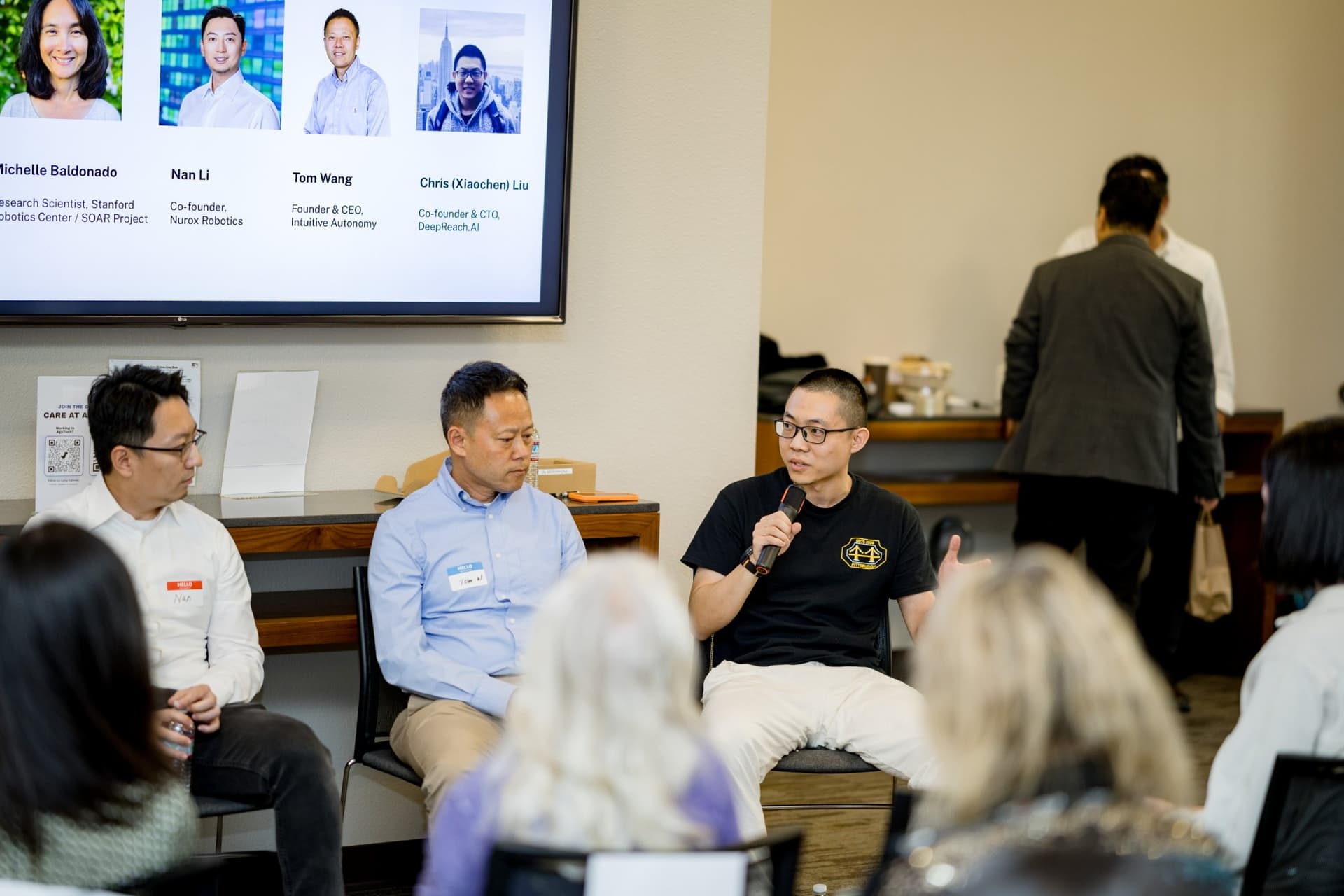 Robotics founder gesturing while speaking during Panel 2 "Robotics for Independent Living" at Care at a Distance: AI, Sensors, Robotics and the Future of Aging, SF Tech Week 2026 at EVGR, Stanford University by JY Studio