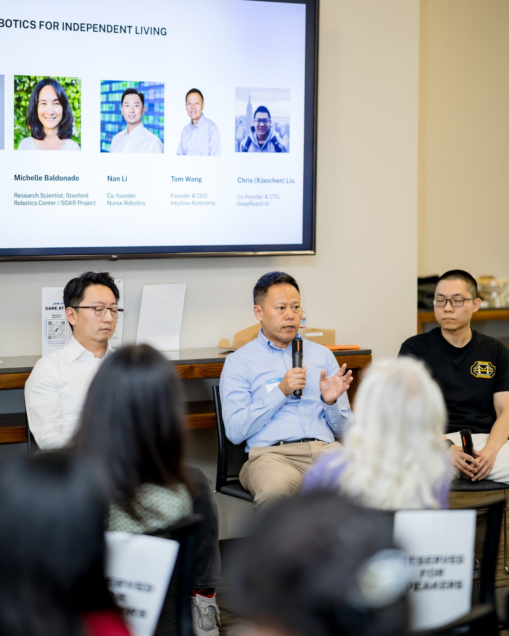 Vertical shot of a panelist in a blue shirt speaking during Panel 2 "Robotics for Independent Living" at Care at a Distance: AI, Sensors, Robotics and the Future of Aging, SF Tech Week 2026 at EVGR, Stanford University by JY Studio