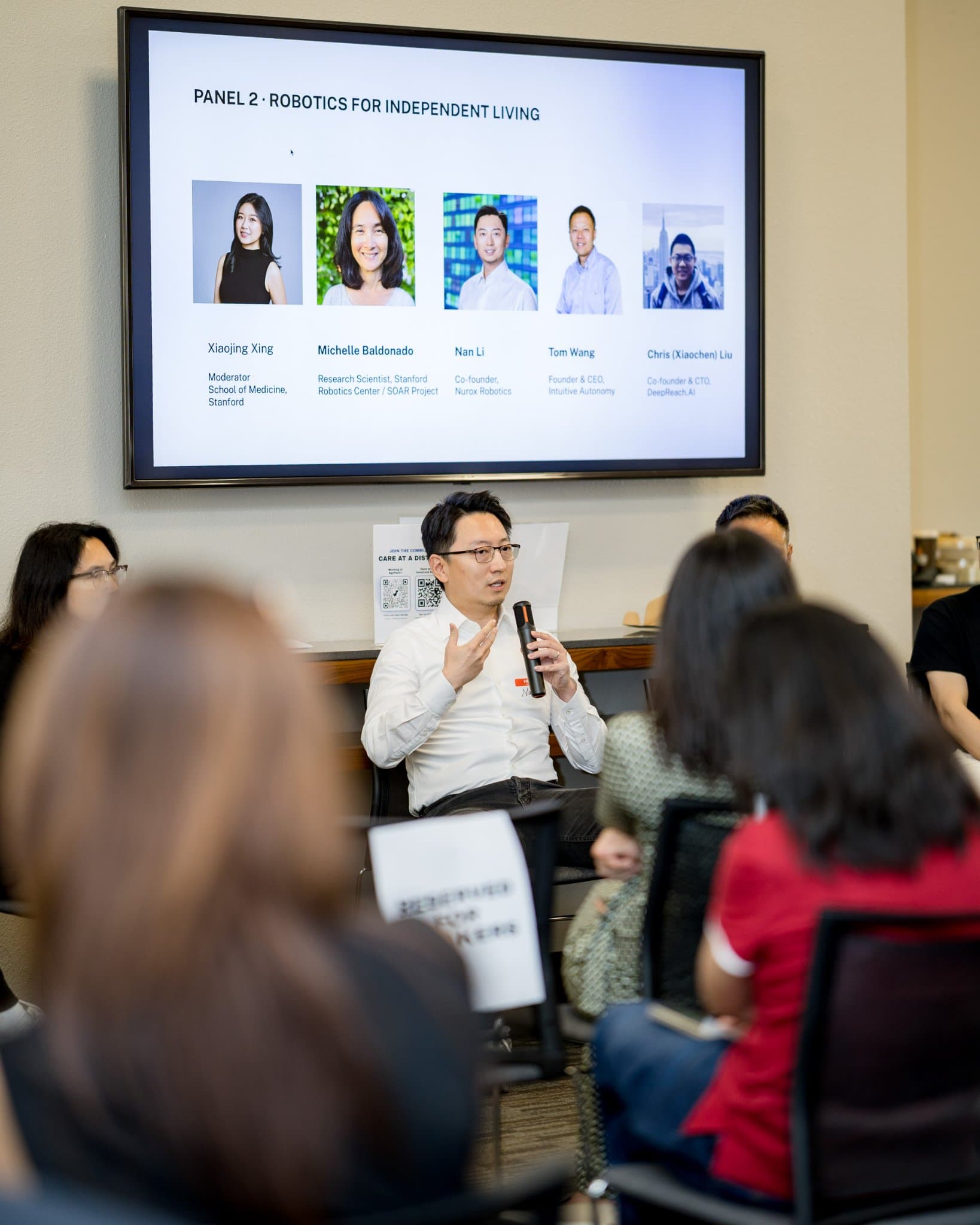 Vertical shot of a panelist speaking under the Panel 2 "Robotics for Independent Living" title slide at Care at a Distance: AI, Sensors, Robotics and the Future of Aging, SF Tech Week 2026 at EVGR, Stanford University by JY Studio