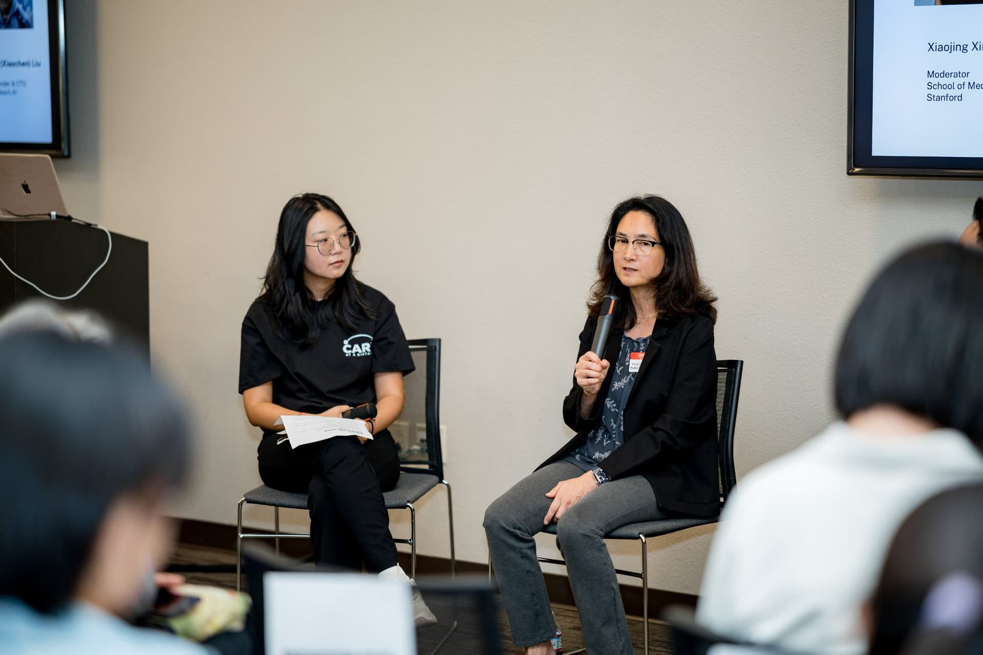 Stanford robotics researcher speaking with a microphone beside the moderator during Panel 2 "Robotics for Independent Living" at Care at a Distance: AI, Sensors, Robotics and the Future of Aging, SF Tech Week 2026 at EVGR, Stanford University by JY Studio