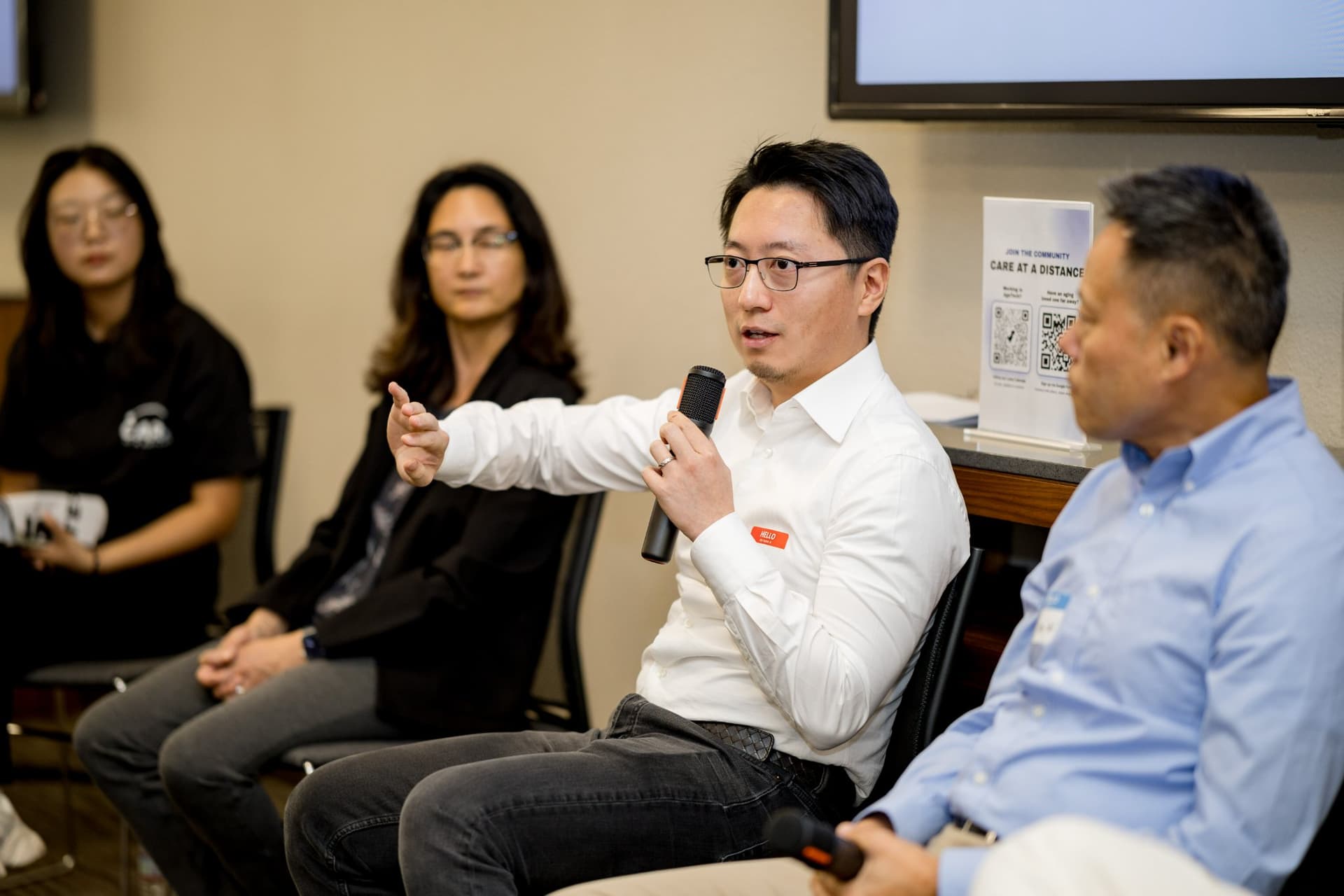 Panelist in a white shirt gesturing toward the audience during Panel 2 "Robotics for Independent Living" at Care at a Distance: AI, Sensors, Robotics and the Future of Aging, SF Tech Week 2026 at EVGR, Stanford University by JY Studio