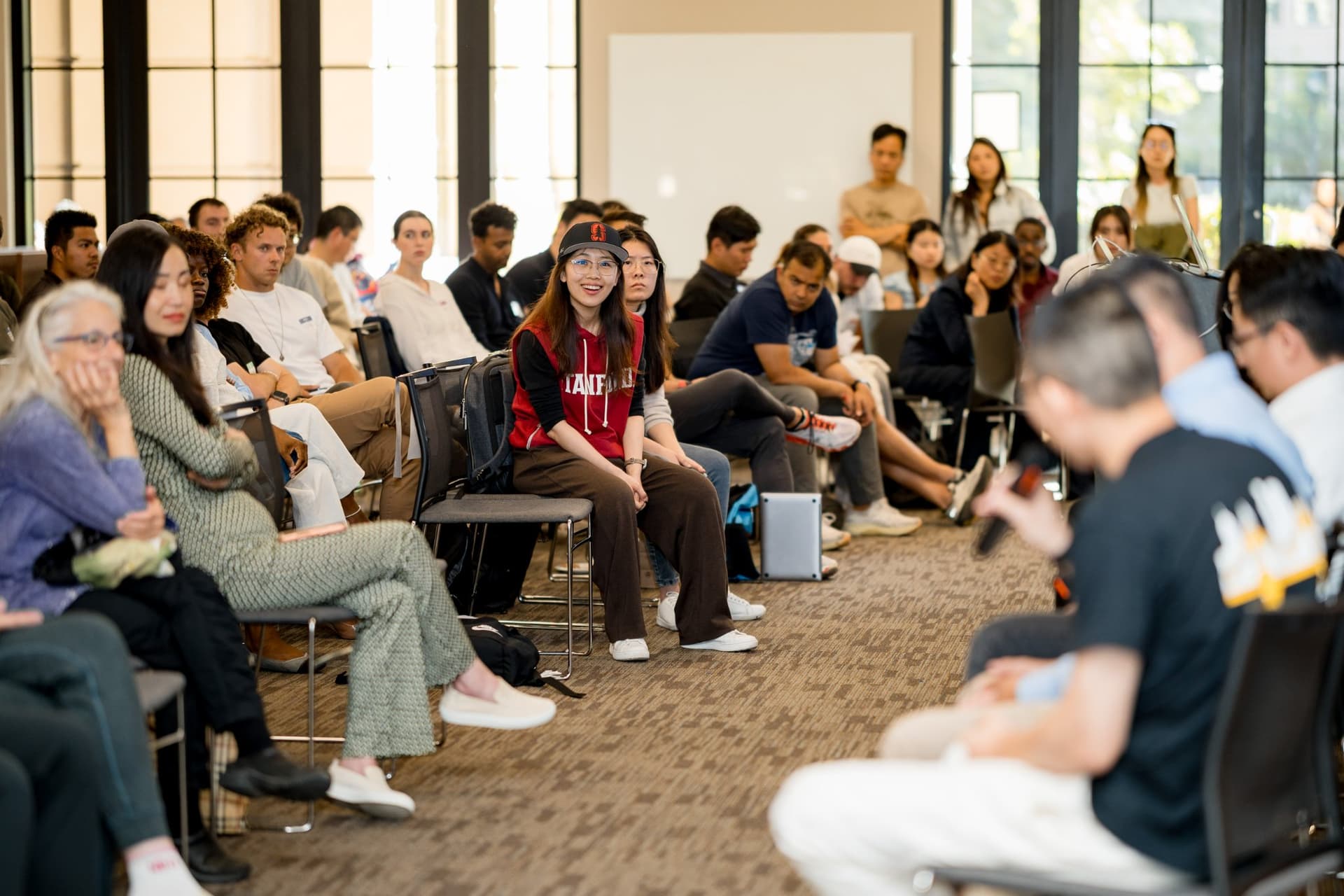 Attendees in a Stanford sweatshirt and the audience smiling at a panelist answer at Care at a Distance: AI, Sensors, Robotics and the Future of Aging, SF Tech Week 2026 at EVGR, Stanford University by JY Studio