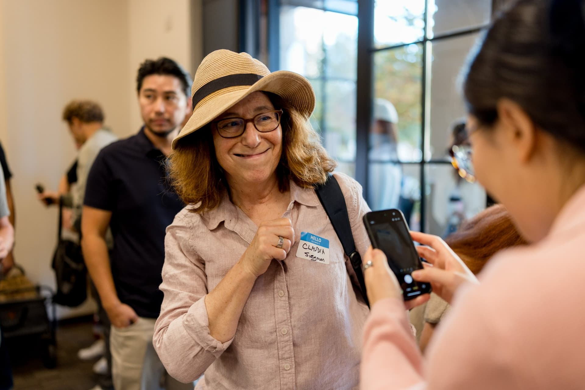 Smiling attendee in a sun hat posing for a photo at check-in at Care at a Distance: AI, Sensors, Robotics and the Future of Aging, SF Tech Week 2026 at EVGR, Stanford University by JY Studio